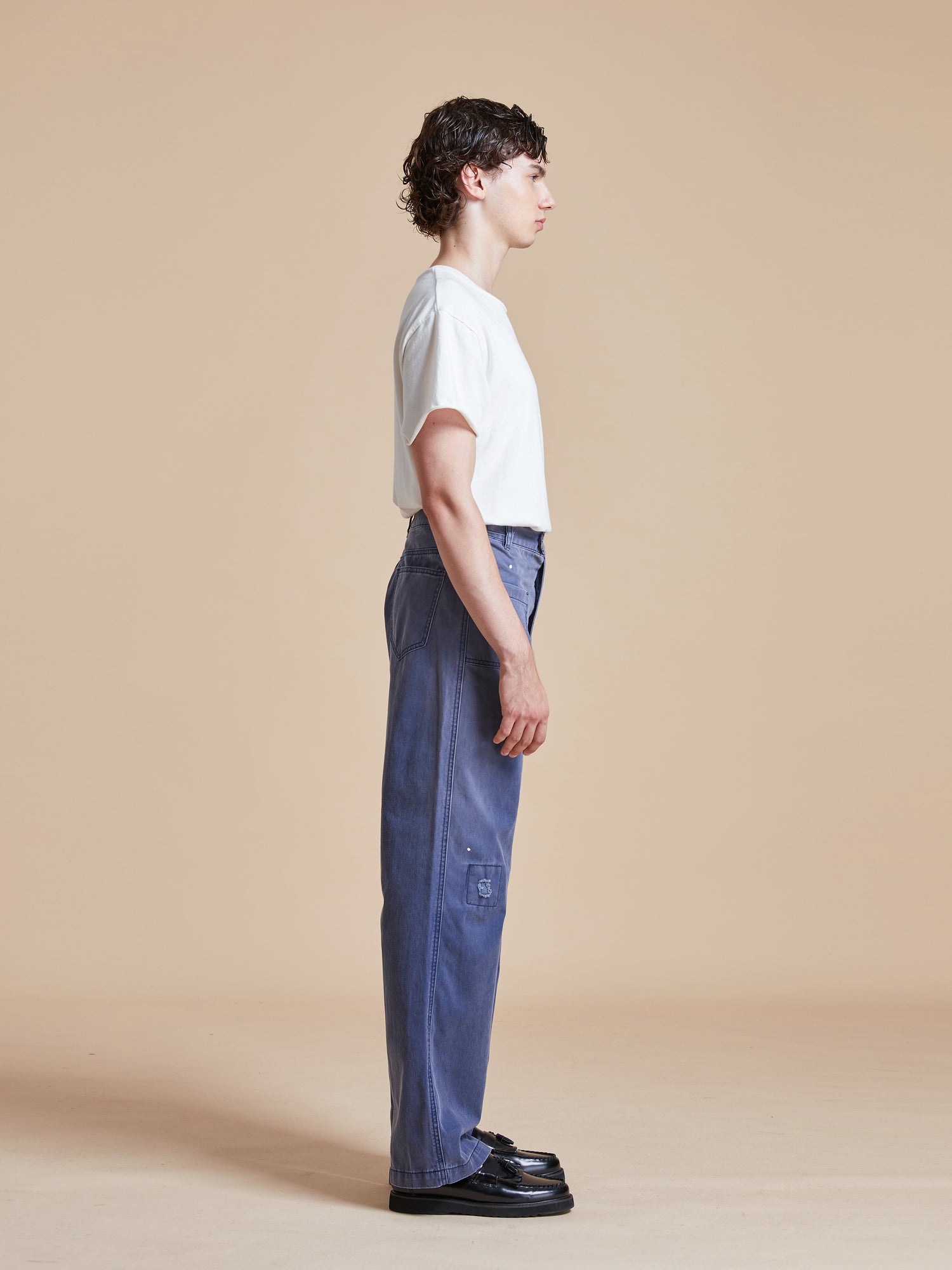 A man wearing a white t-shirt and blue River Painters Chore Pants by Found.