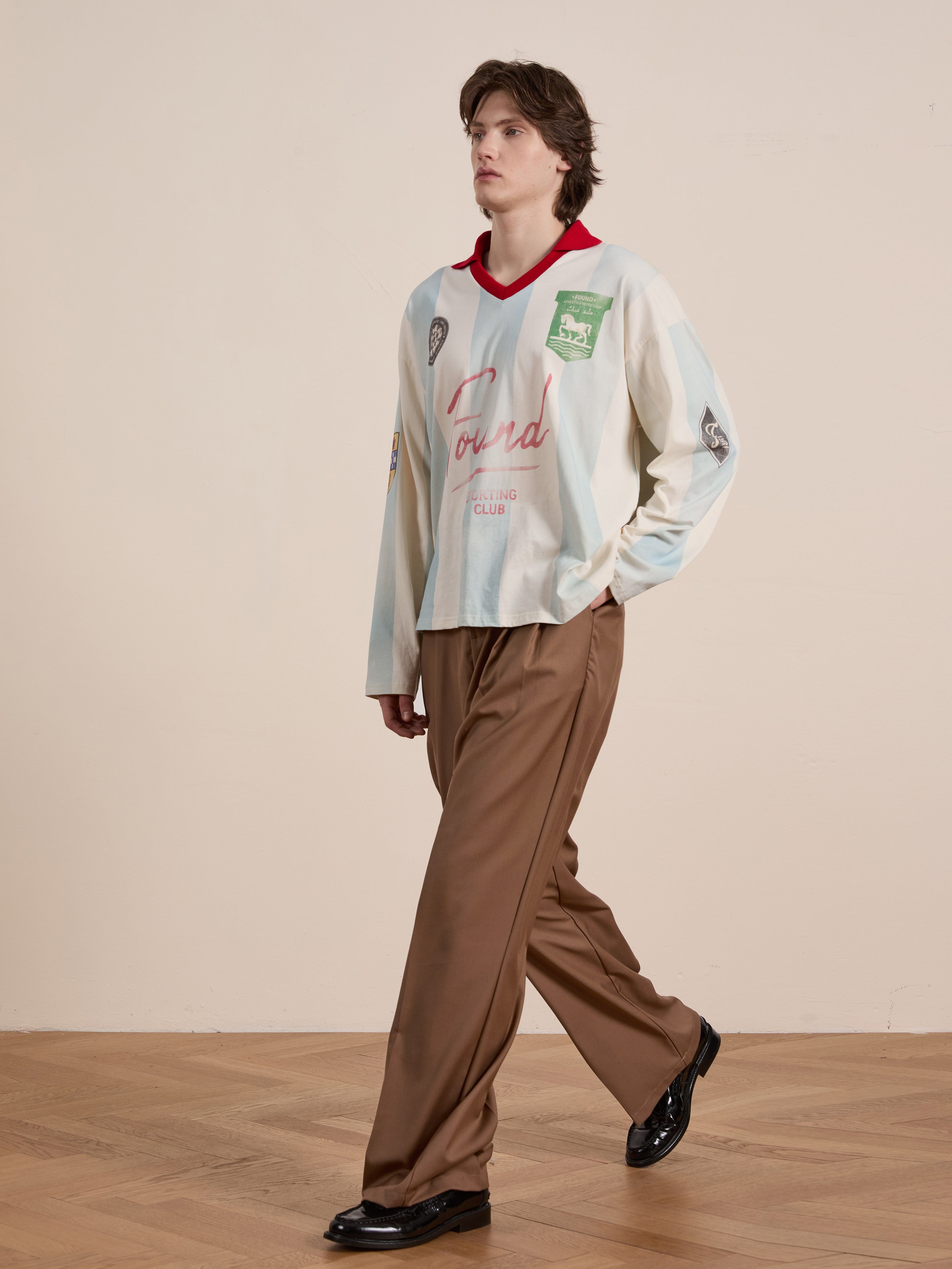 Wearing the Stripe Sport LS Jersey from FOUND and brown wide-leg pants, a person embodies a unisex relaxed fit, walking on a wooden floor with a neutral background.