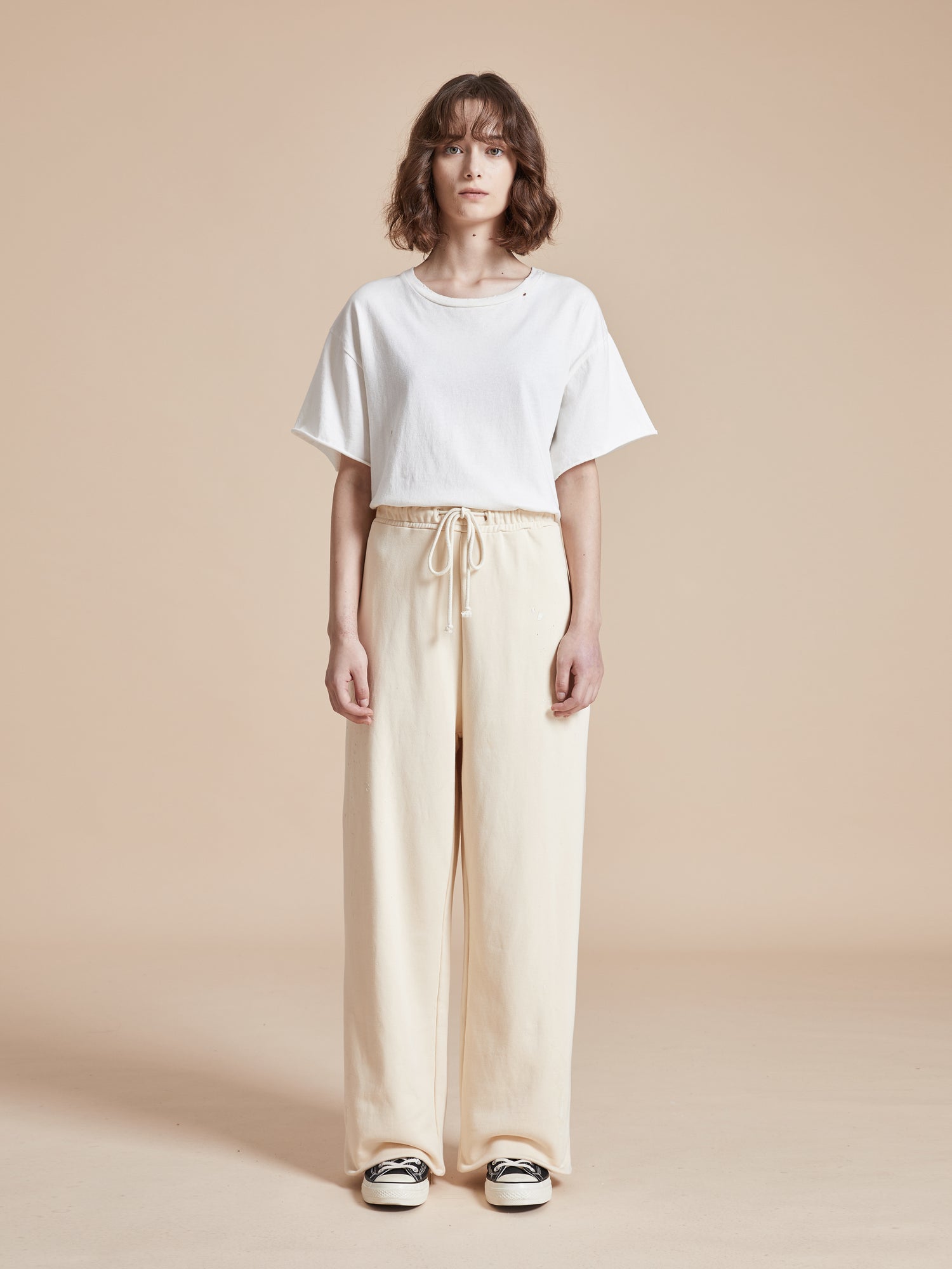 The model is wearing a white t-shirt and Found's Sandshell Lounge Pants with a worn-in look.