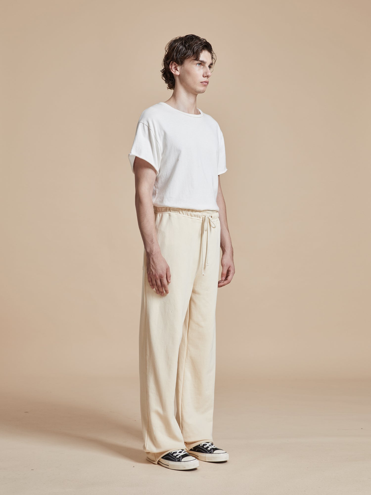 The model is wearing a white t-shirt and beige Found Sandshell Lounge Pants - both wardrobe staples.