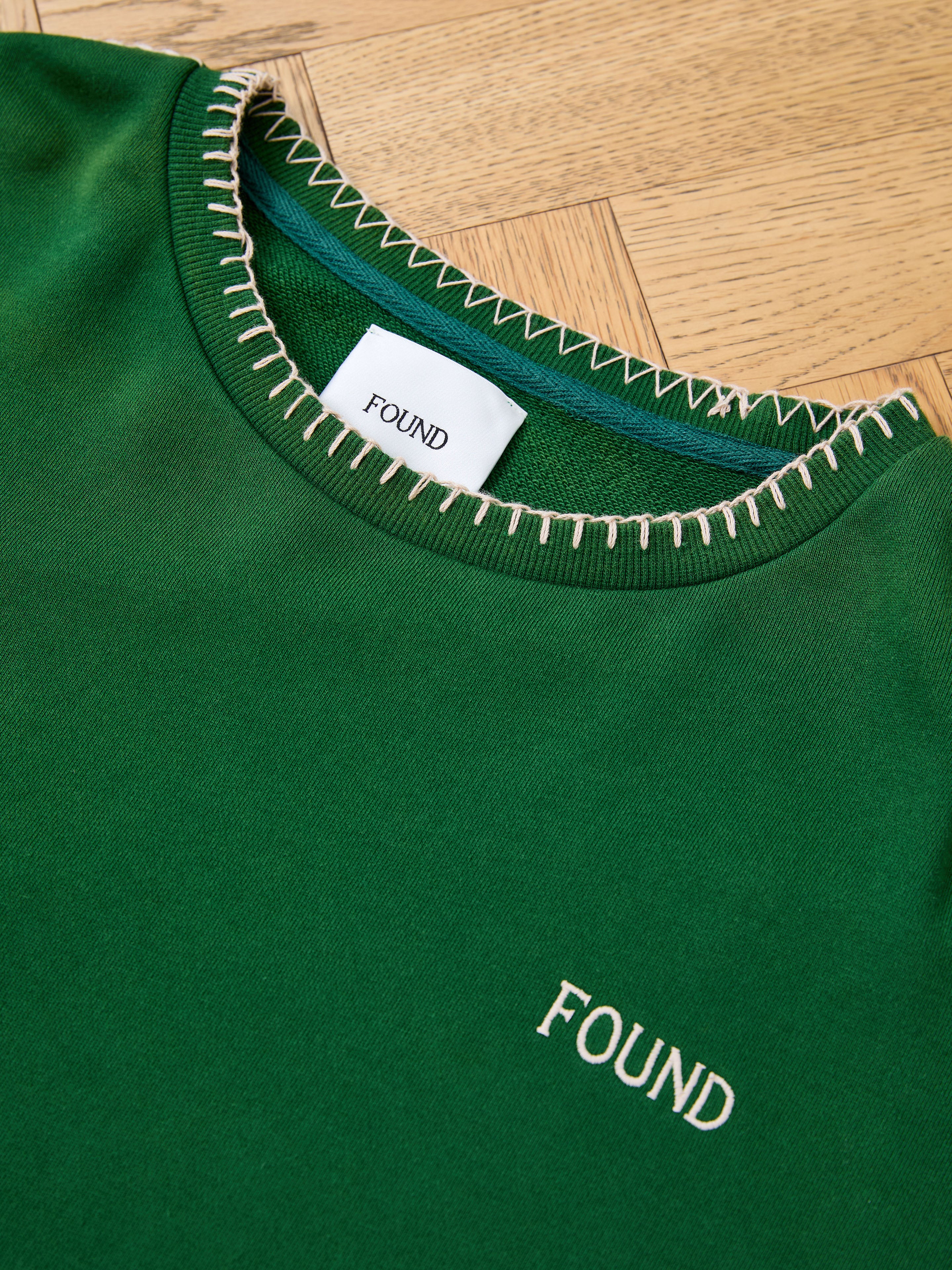 The FOUND Stitched Border Distressed Crewneck features white stitching around the collar and "FOUND" embroidery on the chest. Made from soft French terry cotton, this vintage-style crewneck includes a matching inner collar tag.