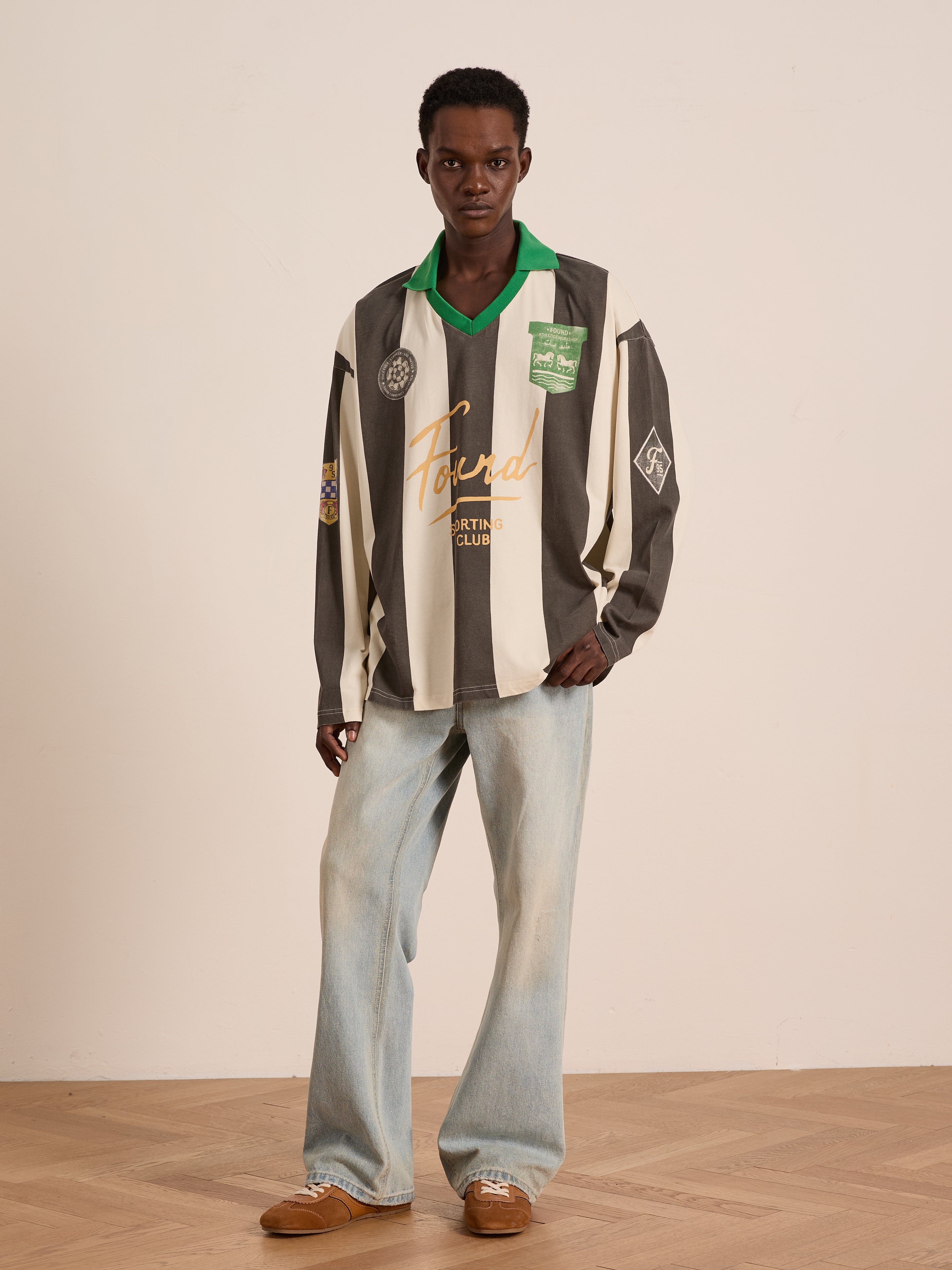 A person stands indoors wearing the FOUND Striped Sport LS Jersey paired with light blue wide-leg jeans and brown shoes. This unisex look combines comfort and style against a plain background.