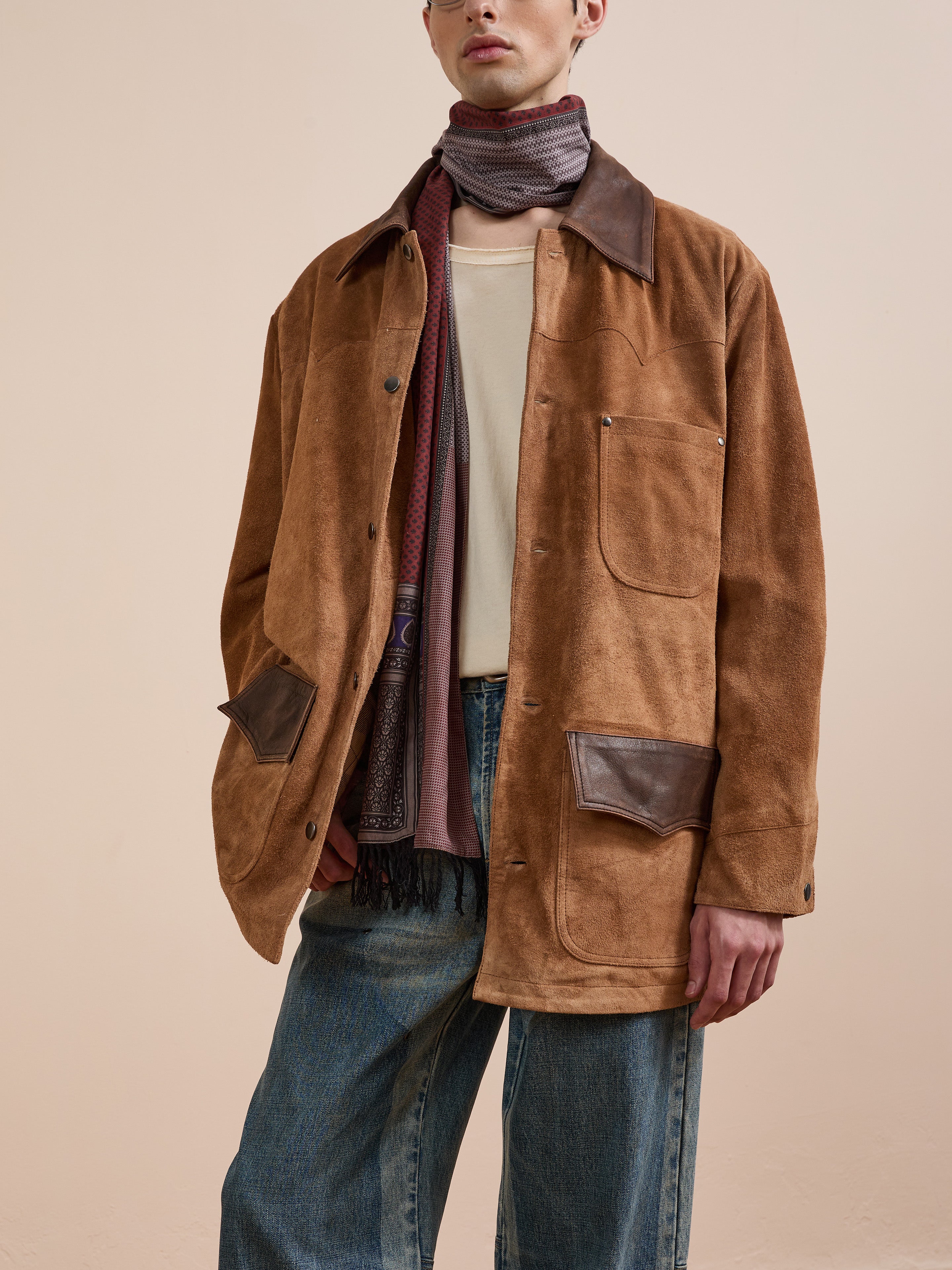 A model in the FOUND Suede Contrast Chore Jacket, paired with a cream shirt, blue jeans, and a patterned scarf, stands against a plain beige background.