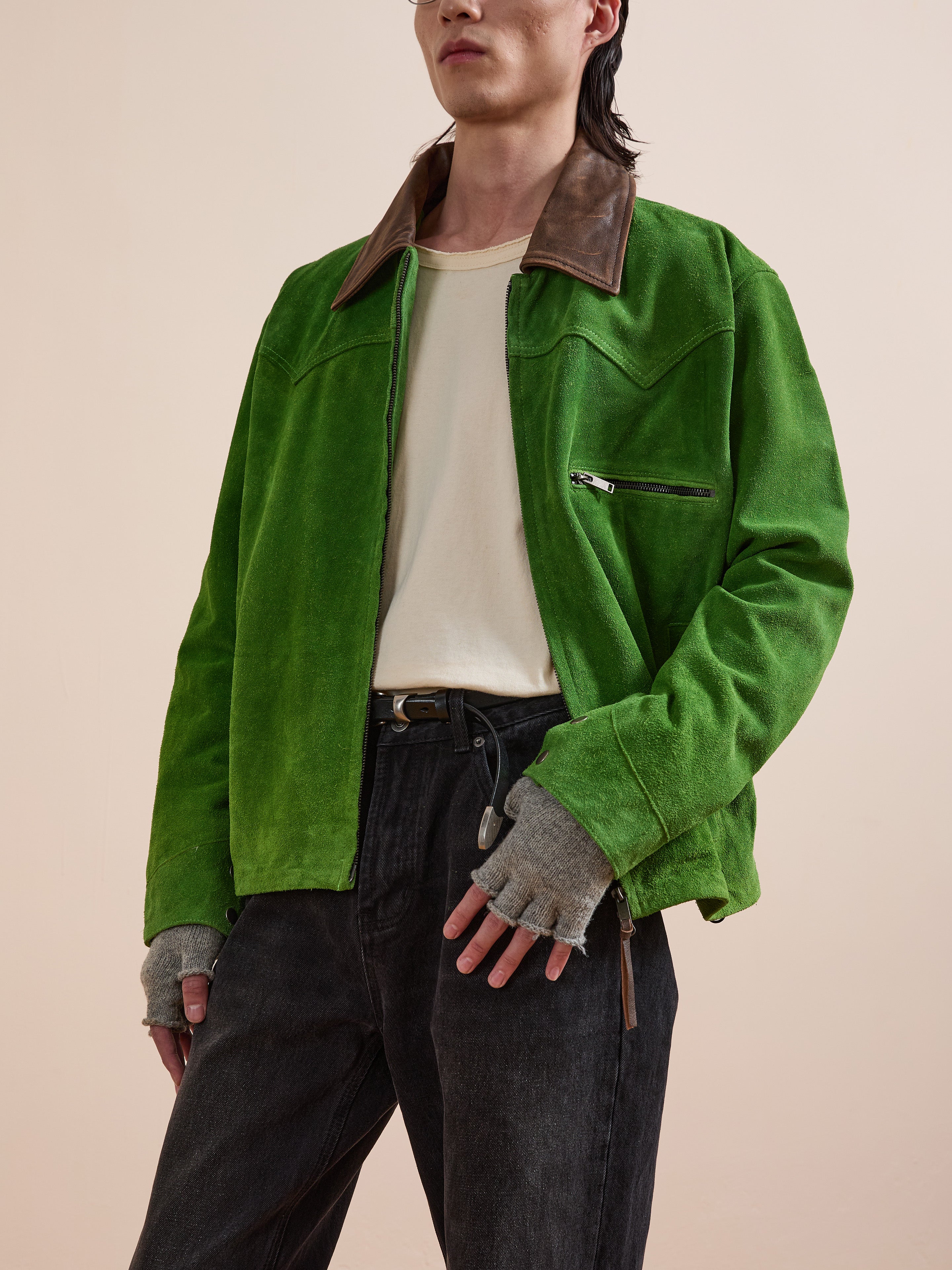 A person stands against a plain background wearing the FOUND Suede Western Barn Jacket with western yoke stitching, a brown collar, paired with a white t-shirt, dark jeans, and gray fingerless gloves.