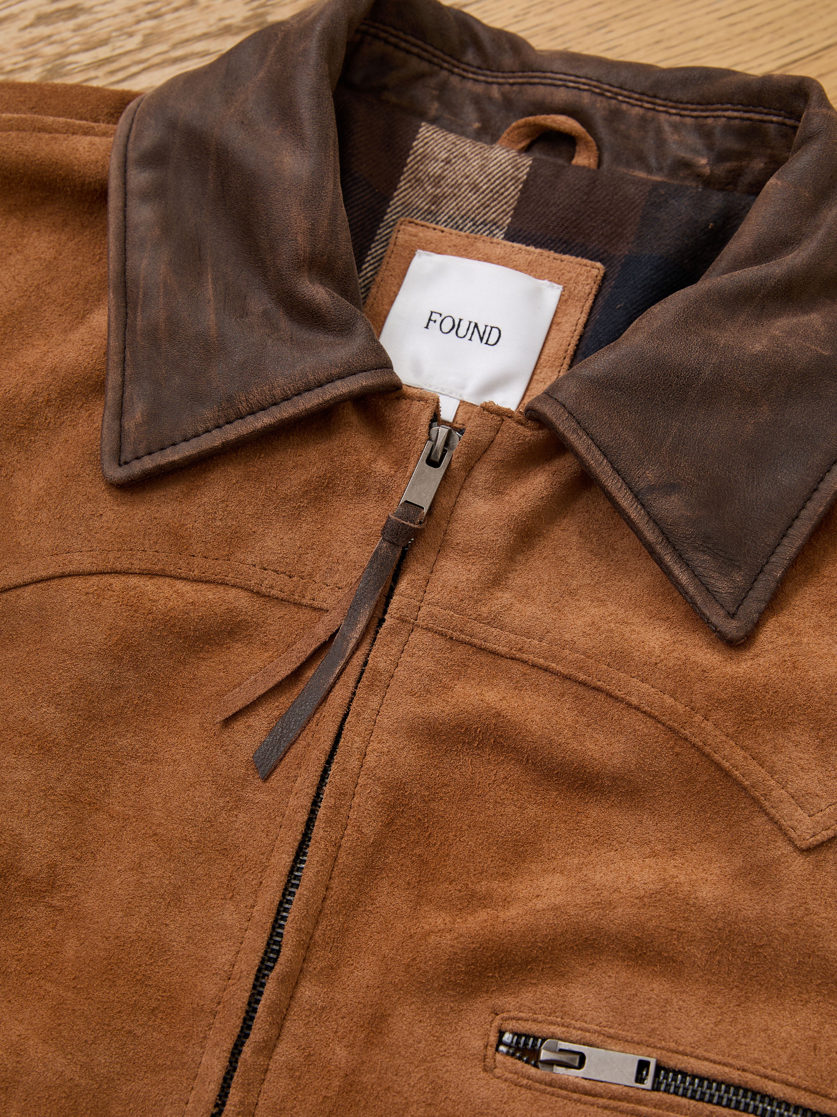 Close-up of the FOUND Suede Western Barn Jacket, featuring brown suede, western yoke stitching, a dark brown leather collar, zipper pocket, and a "FOUND" label sewn inside the neckline.