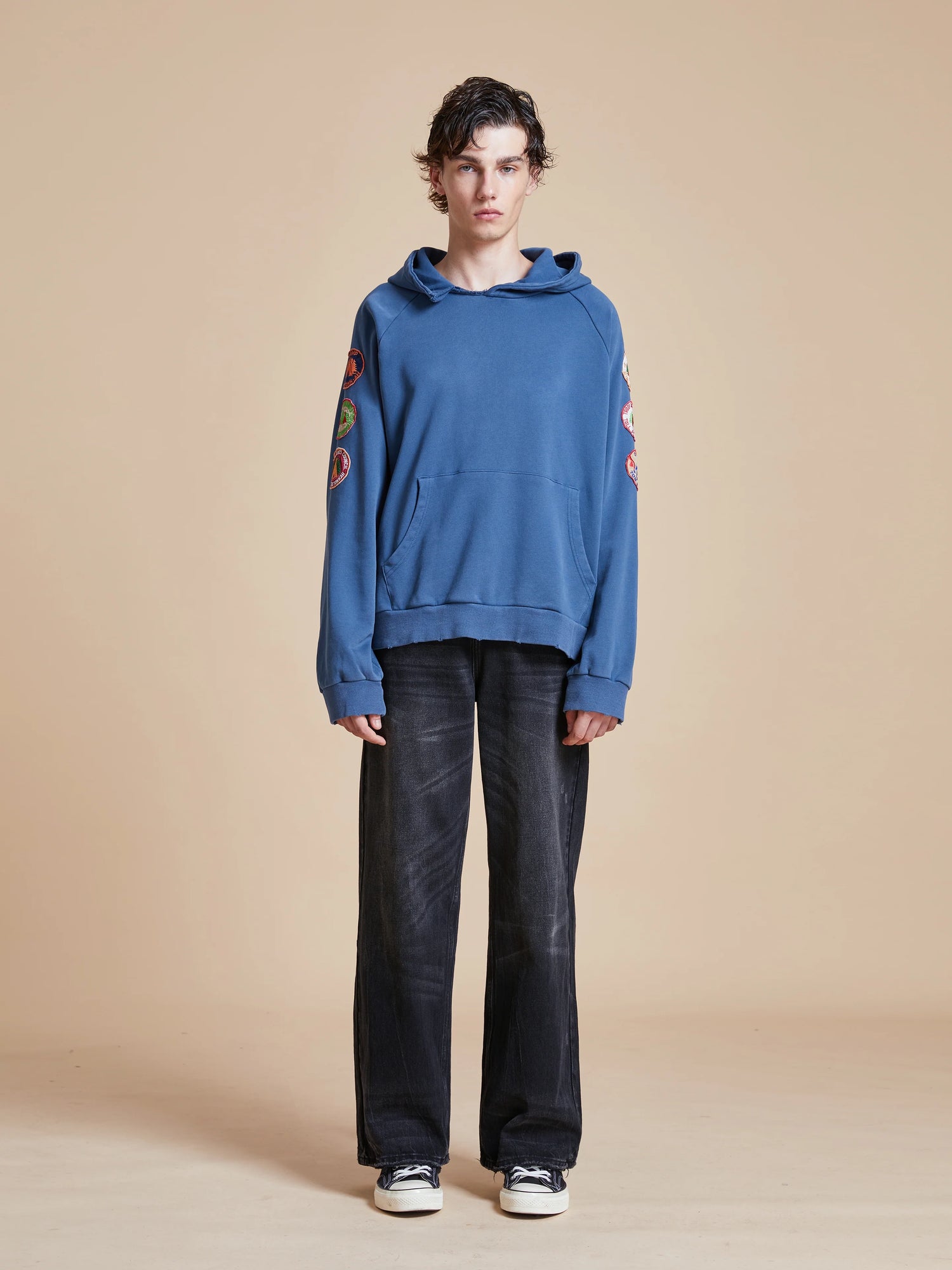 A man wearing a Found Timber Campground Hoodie with vintage-inspired campground patches, and black pants.