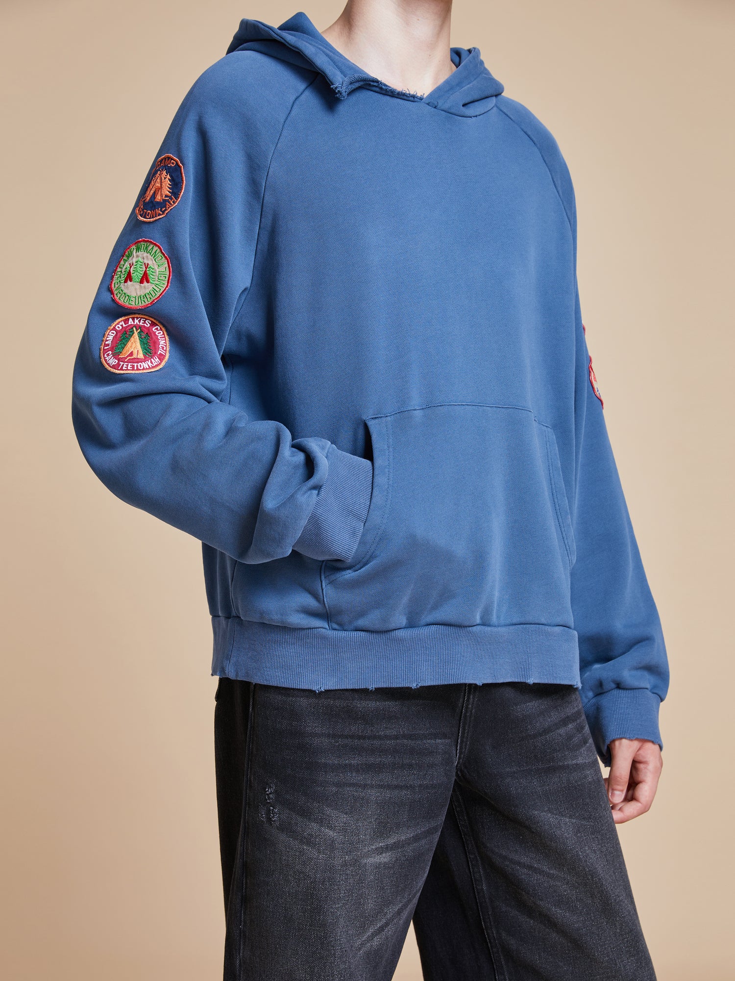 A man wearing a Found Timber Campground Hoodie with patches on it.