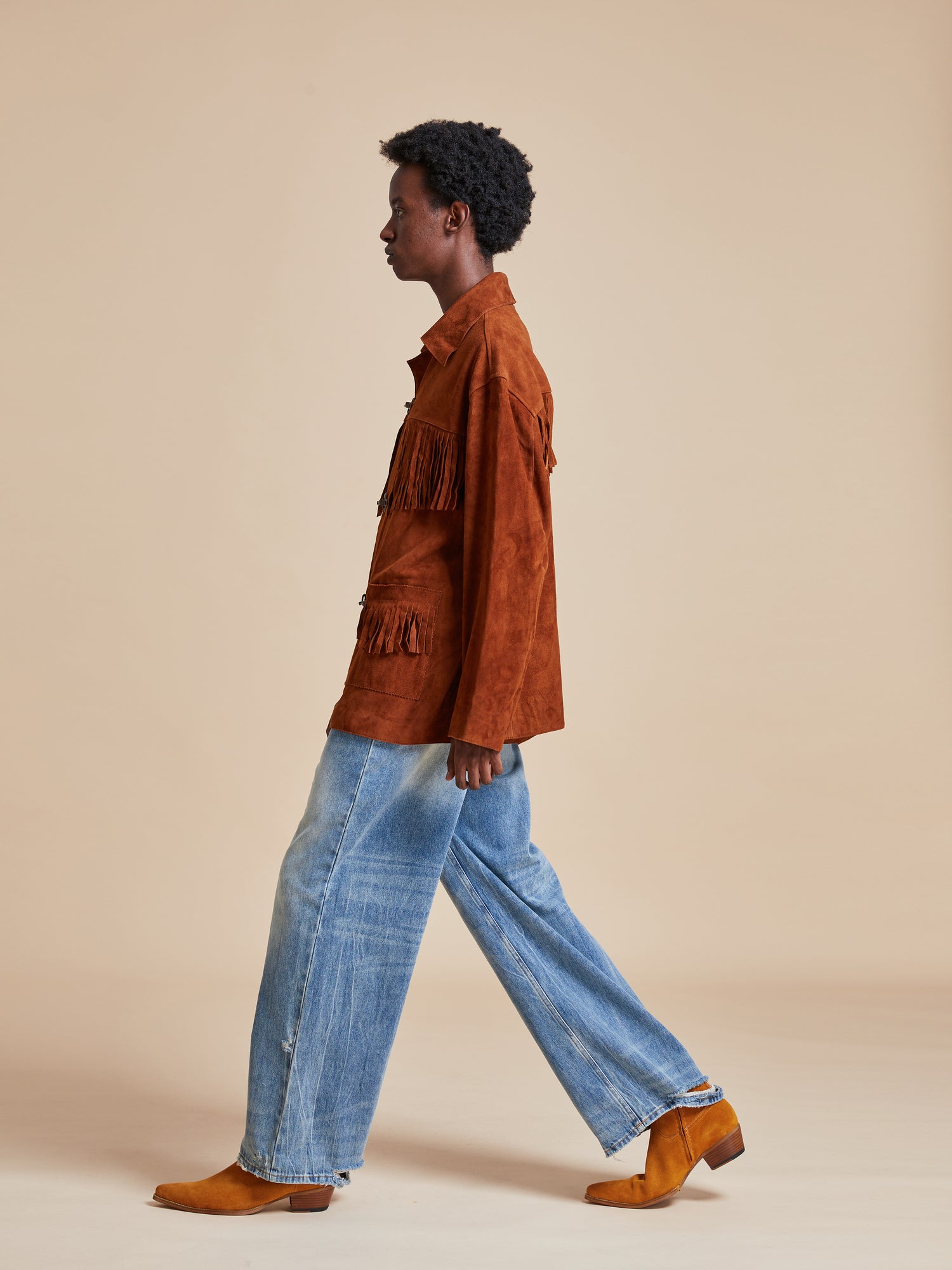 The model is wearing a Found Tobacco Fringe Suede Buckle Jacket and blue jeans.