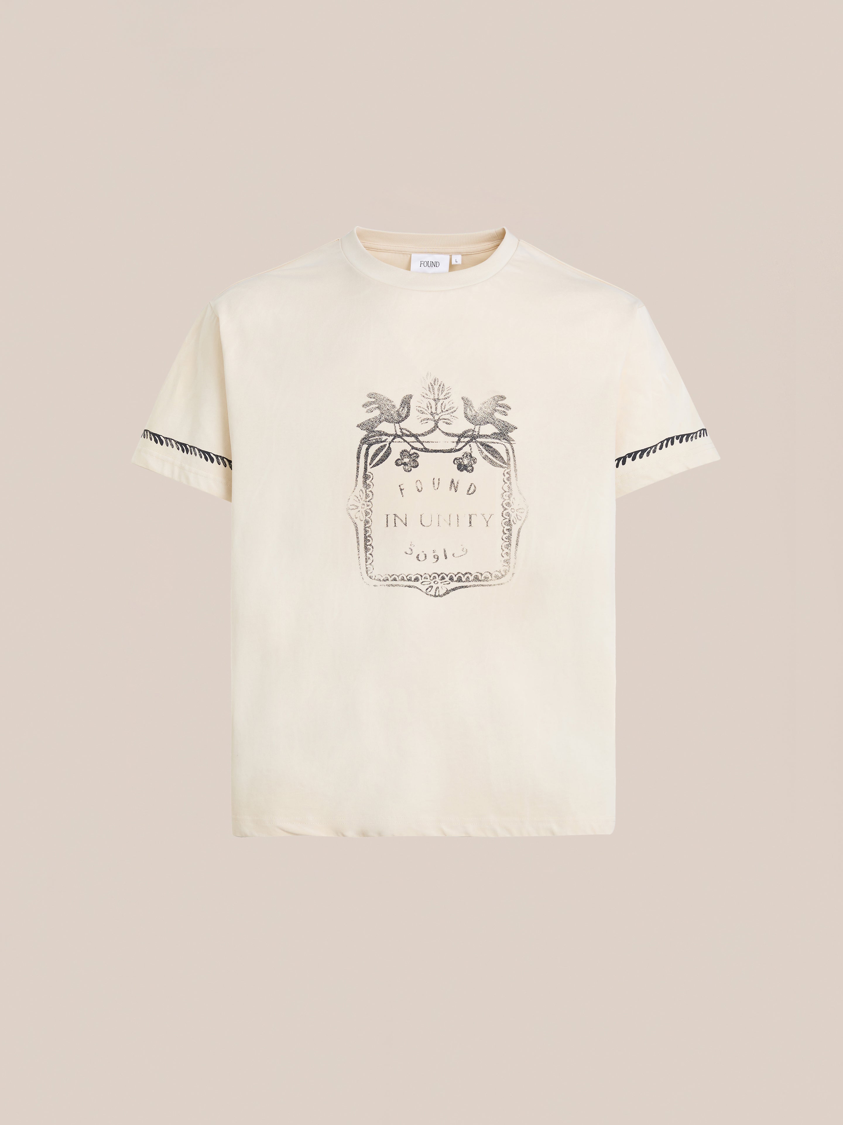 The Unity Crest Tee by FOUND is a cream-colored unisex graphic shirt featuring a decorative crest and "FOUND IN UNITY 3515" on the front, made from mid-weight cotton with black trim on the sleeves.
