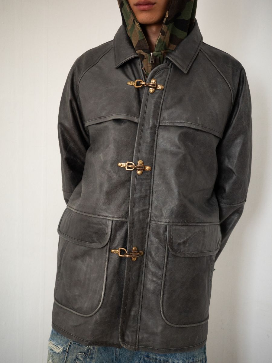 Someone wears the FOUND Distressed Leather Fireman Clasp Jacket over a camouflage hooded sweatshirt and distressed blue jeans.