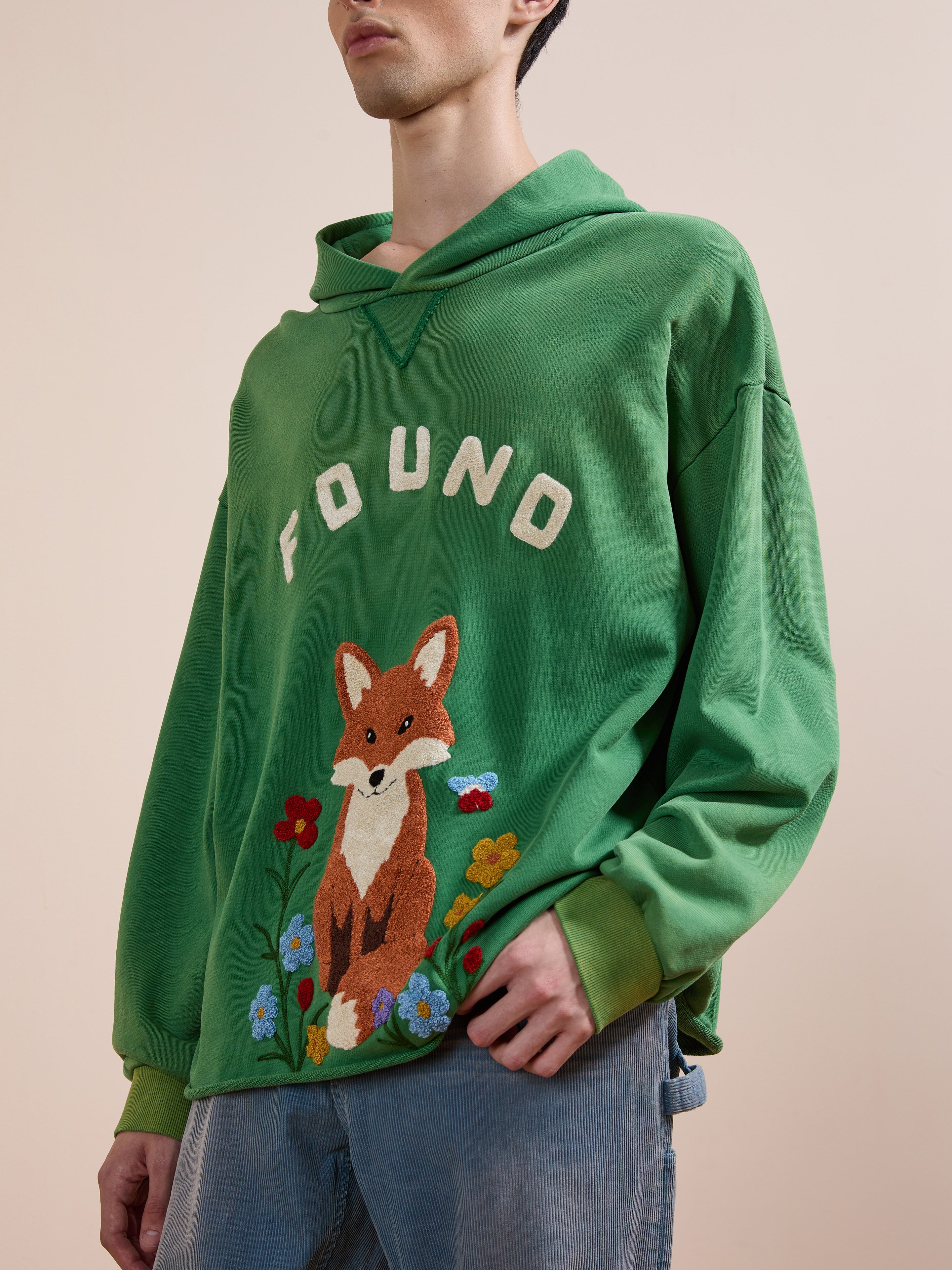 Someone wearing the FOUND Embroidered Wildlife Hoodie, featuring floral embroidery on vintage French-terry cotton, paired with light blue jeans.
