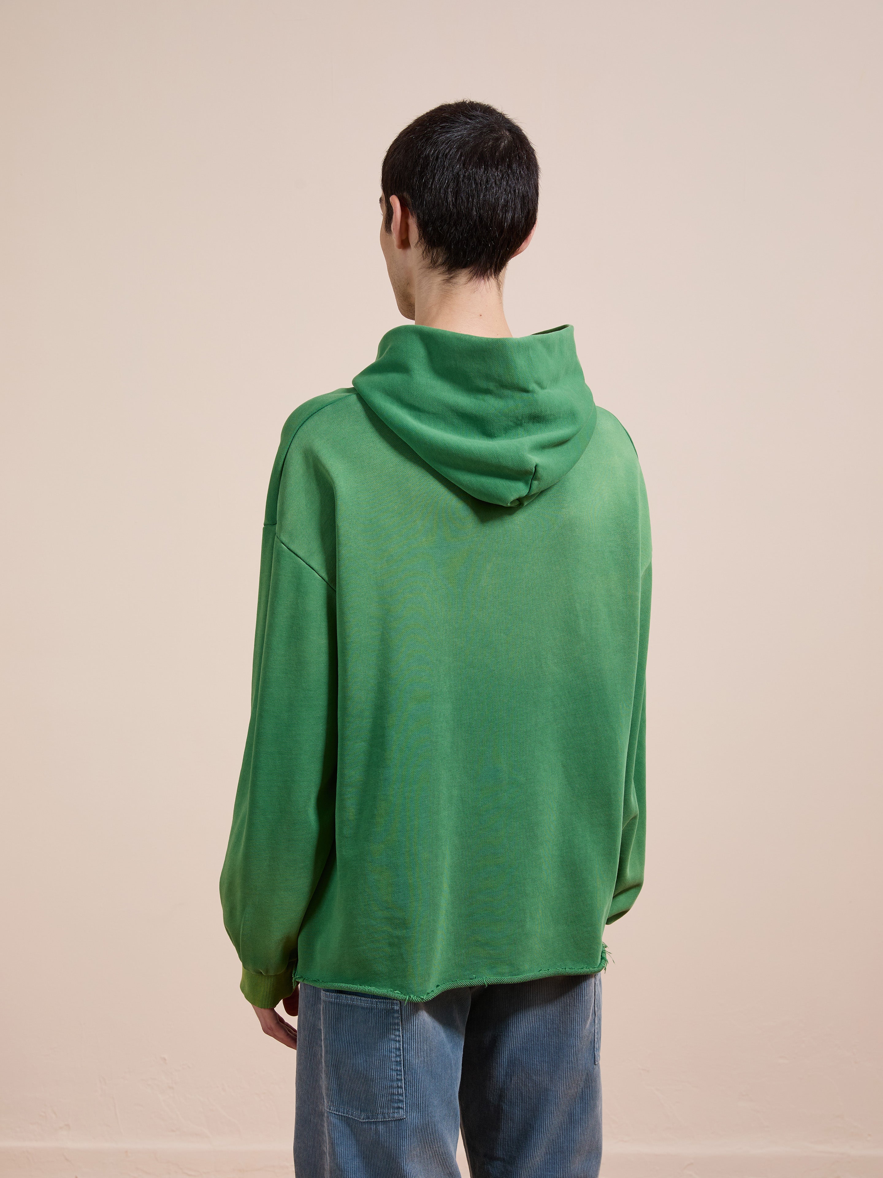 A person with short dark hair wears the FOUND Embroidered Wildlife Hoodie in green vintage French-terry cotton and blue jeans, facing away from the camera against a plain beige background.