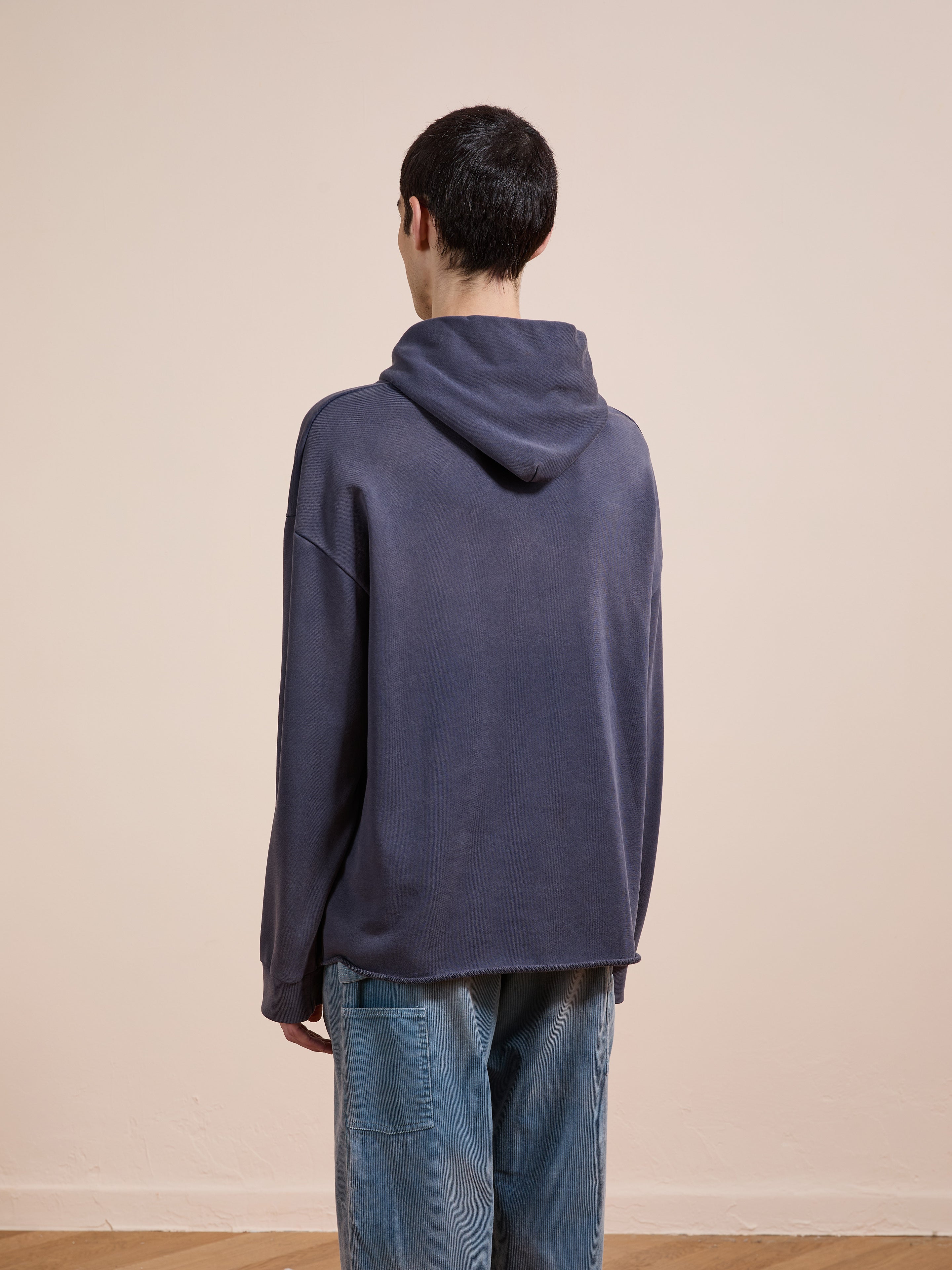 A person stands in front of a wall, wearing the FOUND Embroidered Wildlife Hoodie crafted from vintage French-terry cotton.