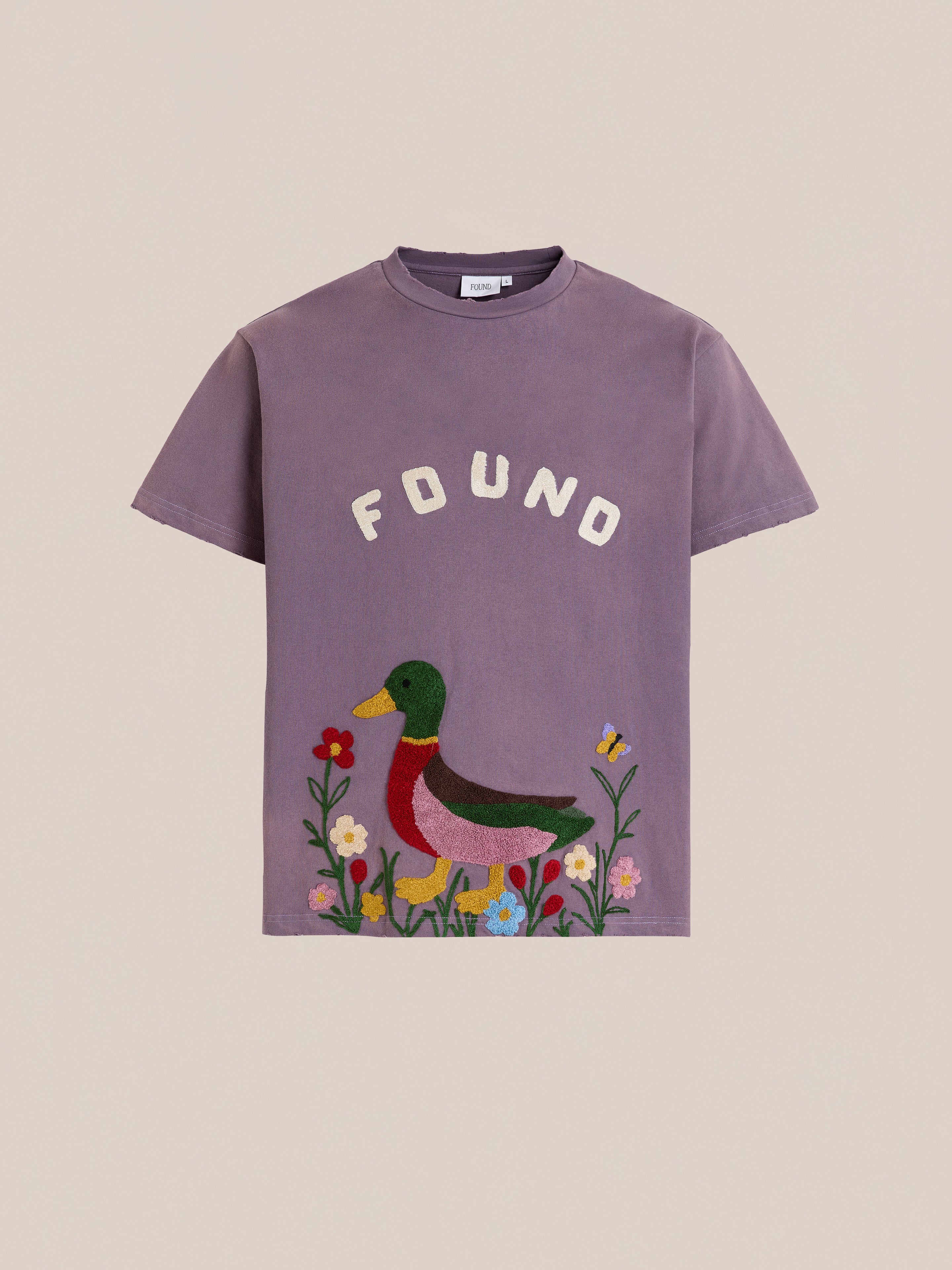 The FOUND Embroidered Wildlife Tee is a purple shirt featuring "FOUND" above a duck, flowers, and a butterfly in vibrant chenille embroidery—ideal for wildlife t-shirt fans.