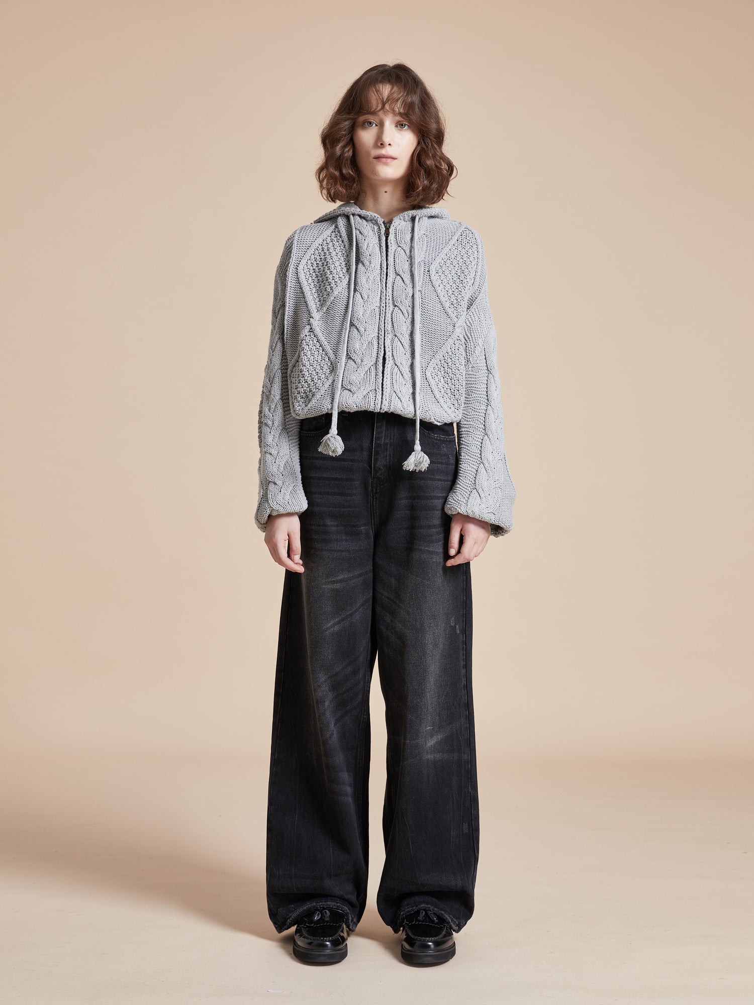 The model is wearing a Zip Up Distressed Cable Knit Hoodie by Found for warmth and comfort.