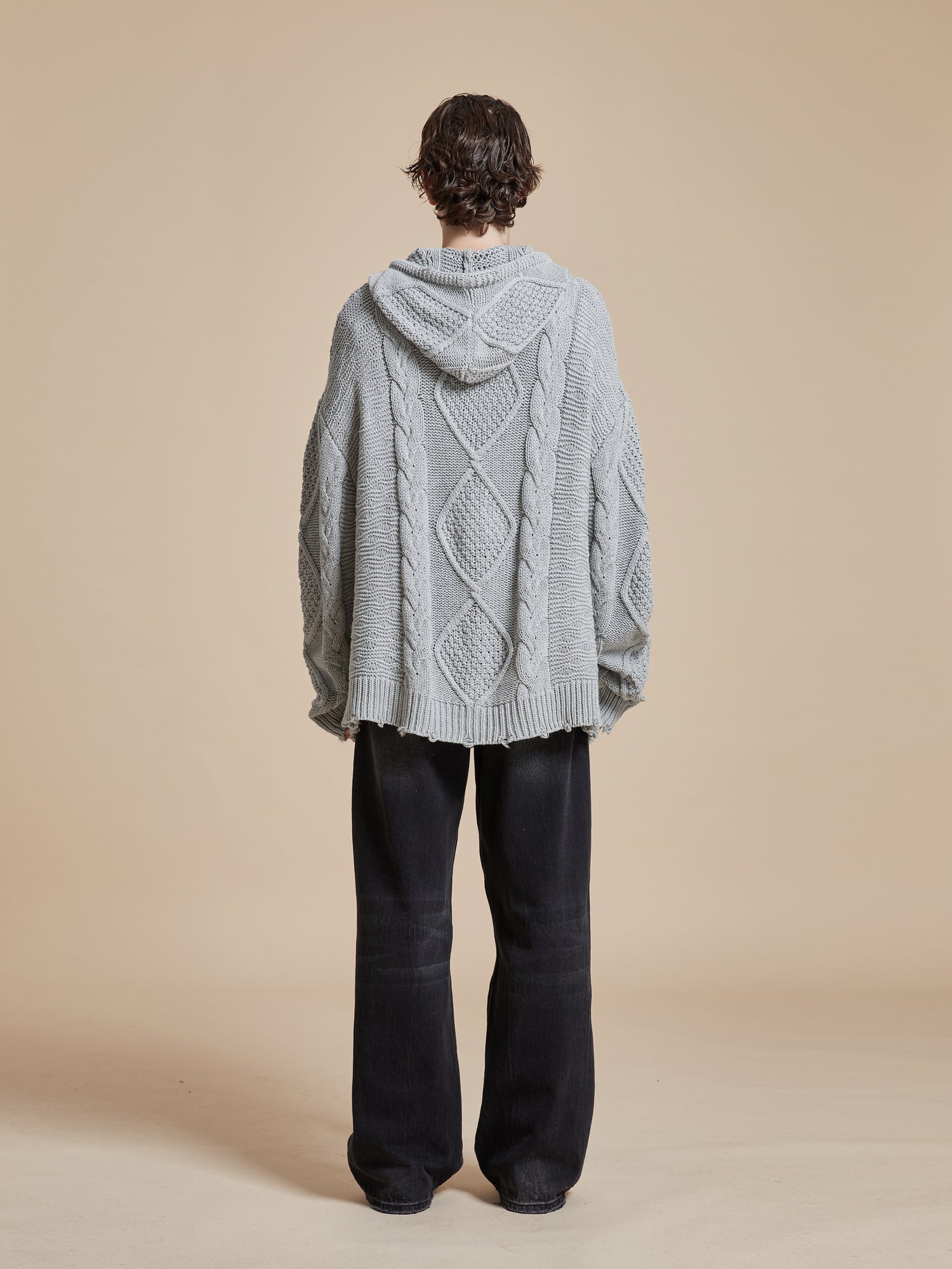 A man wearing a Zip Up Distressed Cable Knit Hoodie from Found exudes warmth and comfort.