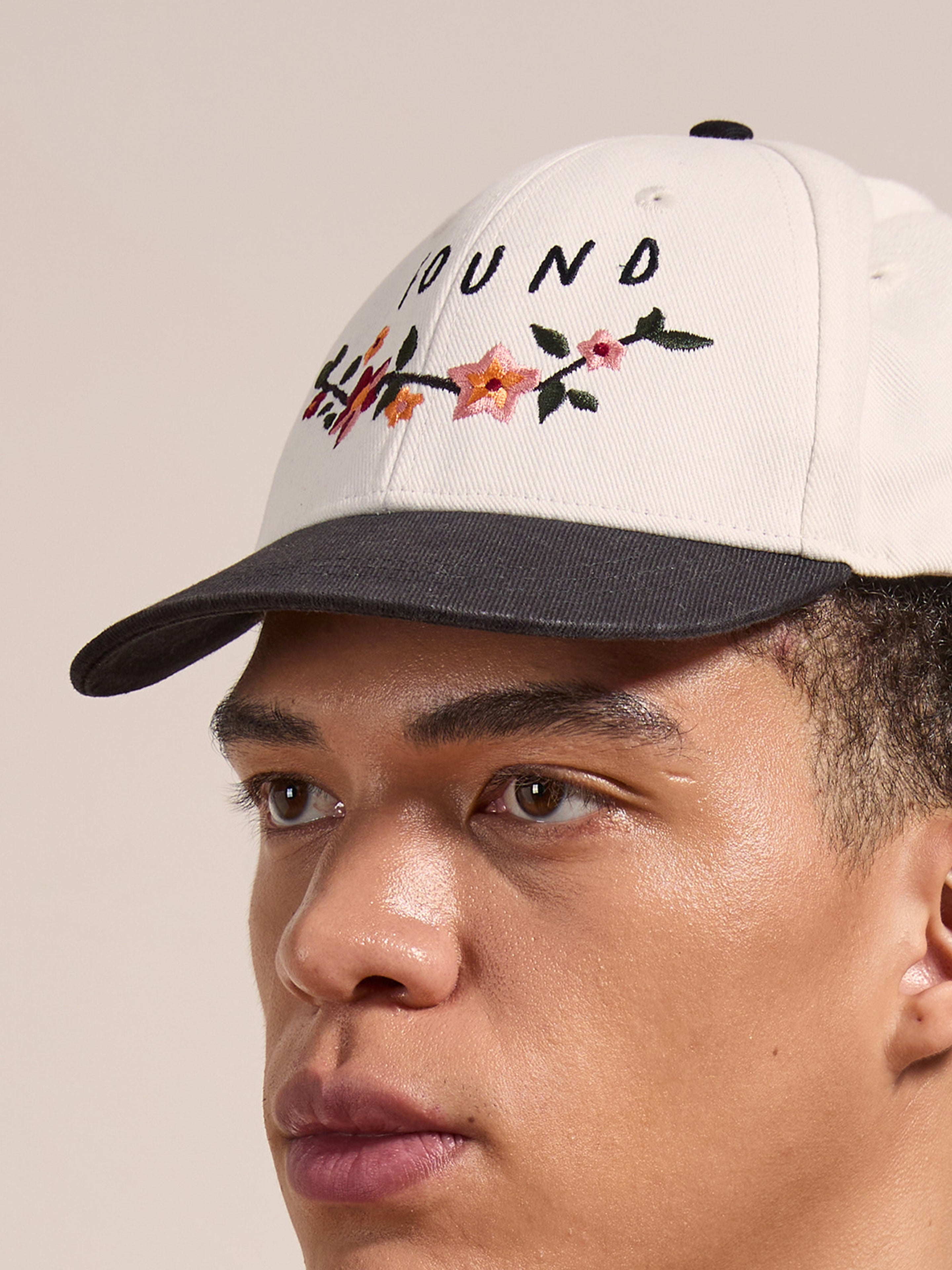A close-up of a person wearing the FOUND Greenlands Contrast Cap, featuring white and black panels, floral Kantha-style embroidery, and partially visible text on the curved brim.