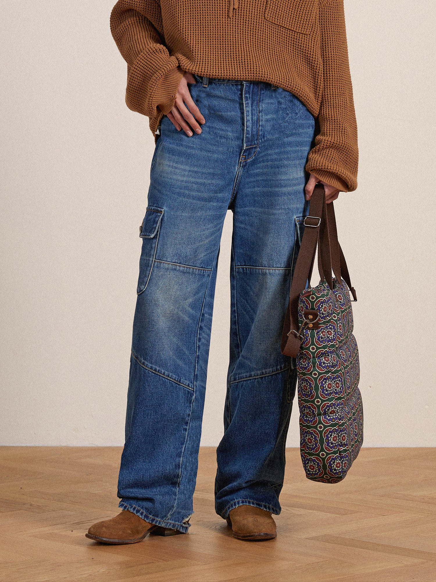Person standing in Found Siwa Cargo Paneled Jeans with cargo pockets and a brown sweater, holding a patterned bag, against a neutral background.