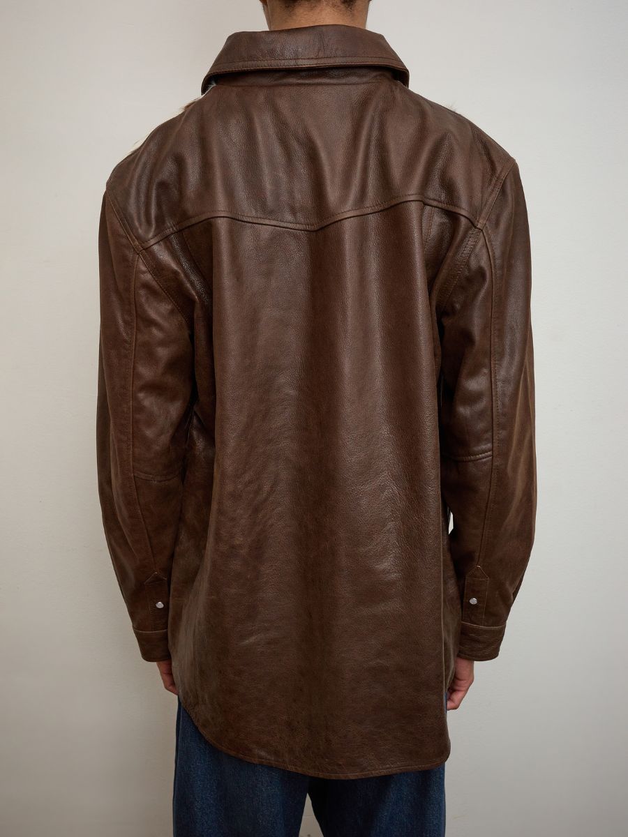A person wearing the FOUND Distressed Leather Cowhide Contrast Western Shirt, seen from behind with blue jeans, stands against a plain light-colored wall.