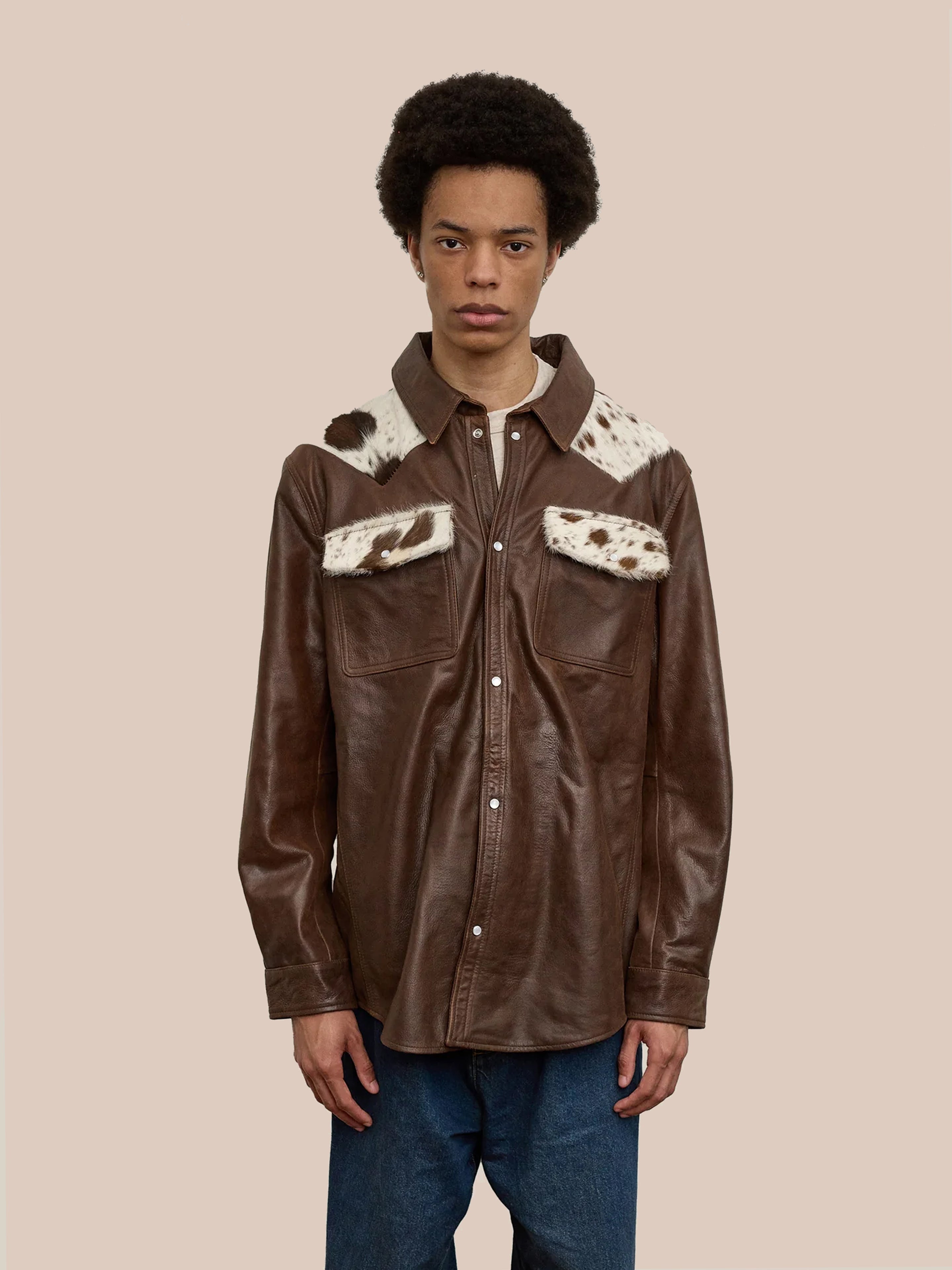 A person wears the FOUND Distressed Leather Cowhide Contrast Western Shirt, featuring genuine cowhide with white and brown fur accents on the shoulders and chest pockets, set against a plain beige background for a rustic yet timeless unisex look.