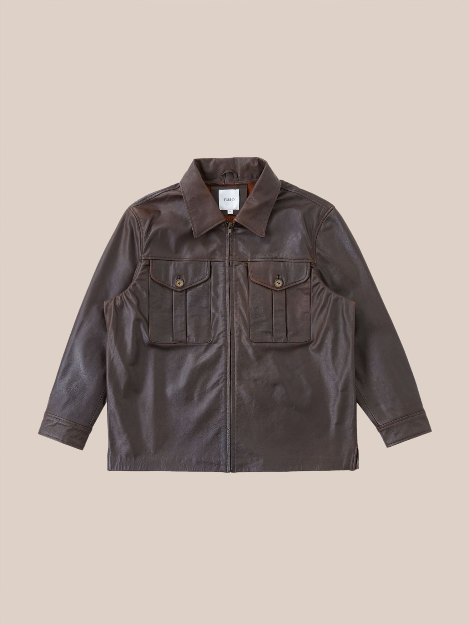 Sepia Leather Overshirt by Found, with a collared neckline and two chest pockets displayed against a pale pink background.