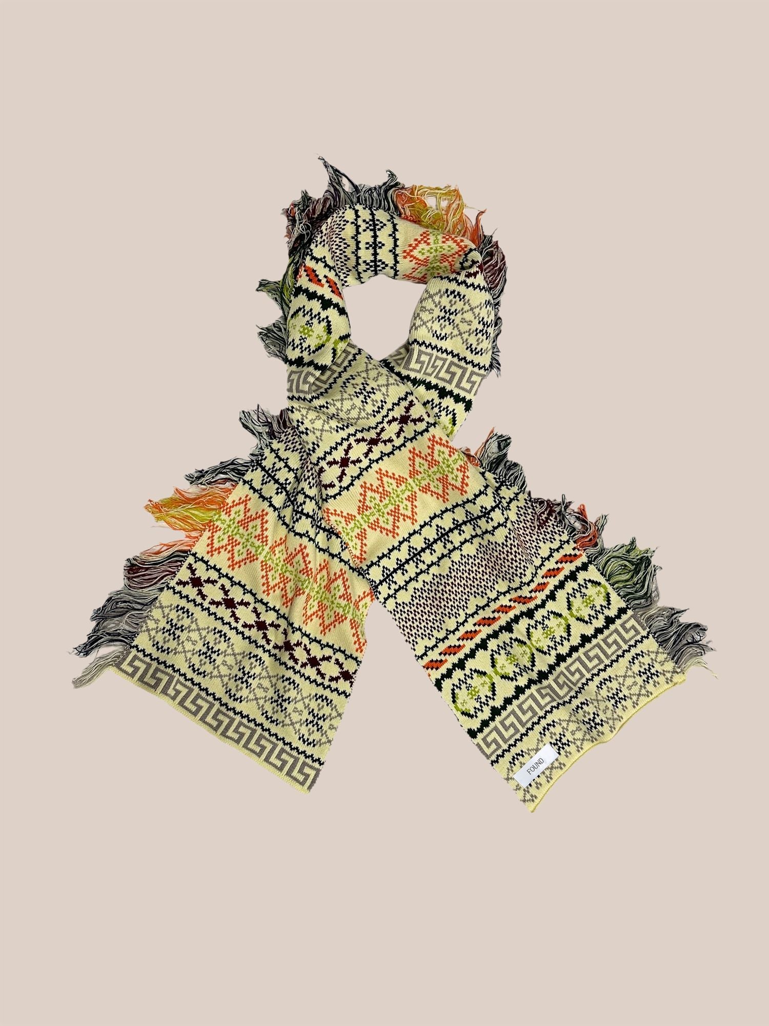 A colorful, patterned Isles Scarf from Found with fringed ends, displayed on a light pink background.
