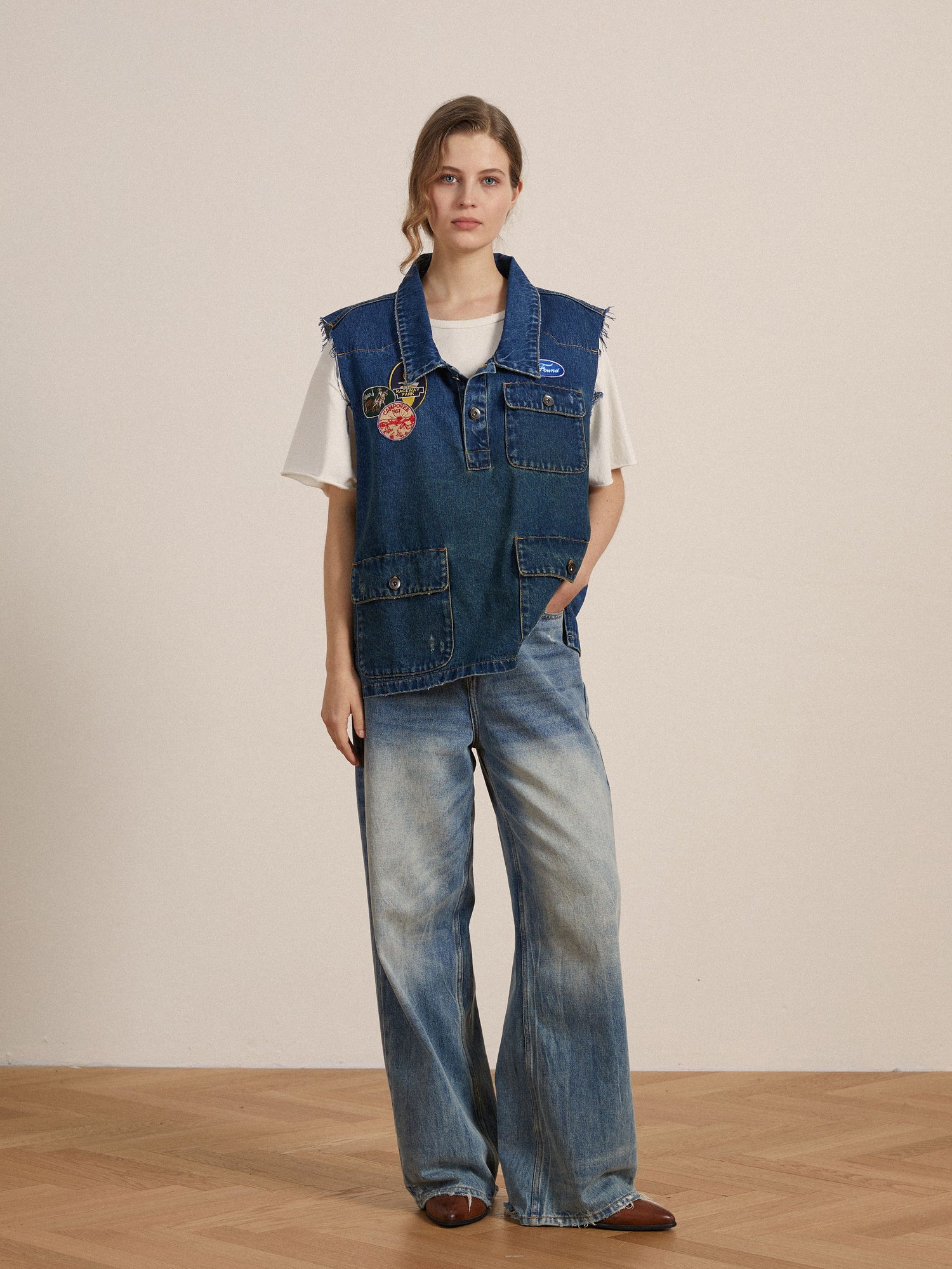 A woman wearing a Found Raw Cut Patch Mechanic Denim vest adorned with embroidered patches and wide leg pants.