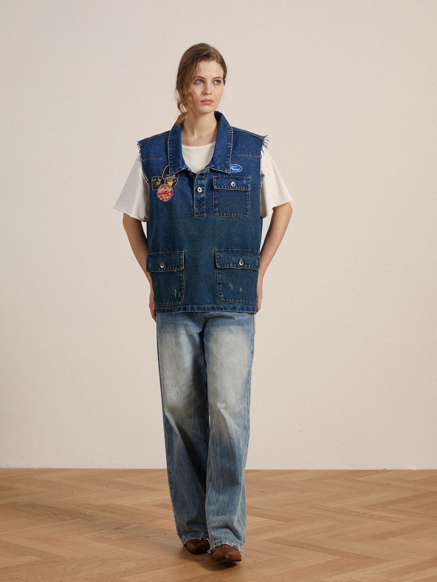 A woman in a Found Raw Cut Patch Mechanic Denim Vest adorned with embroidered patches.