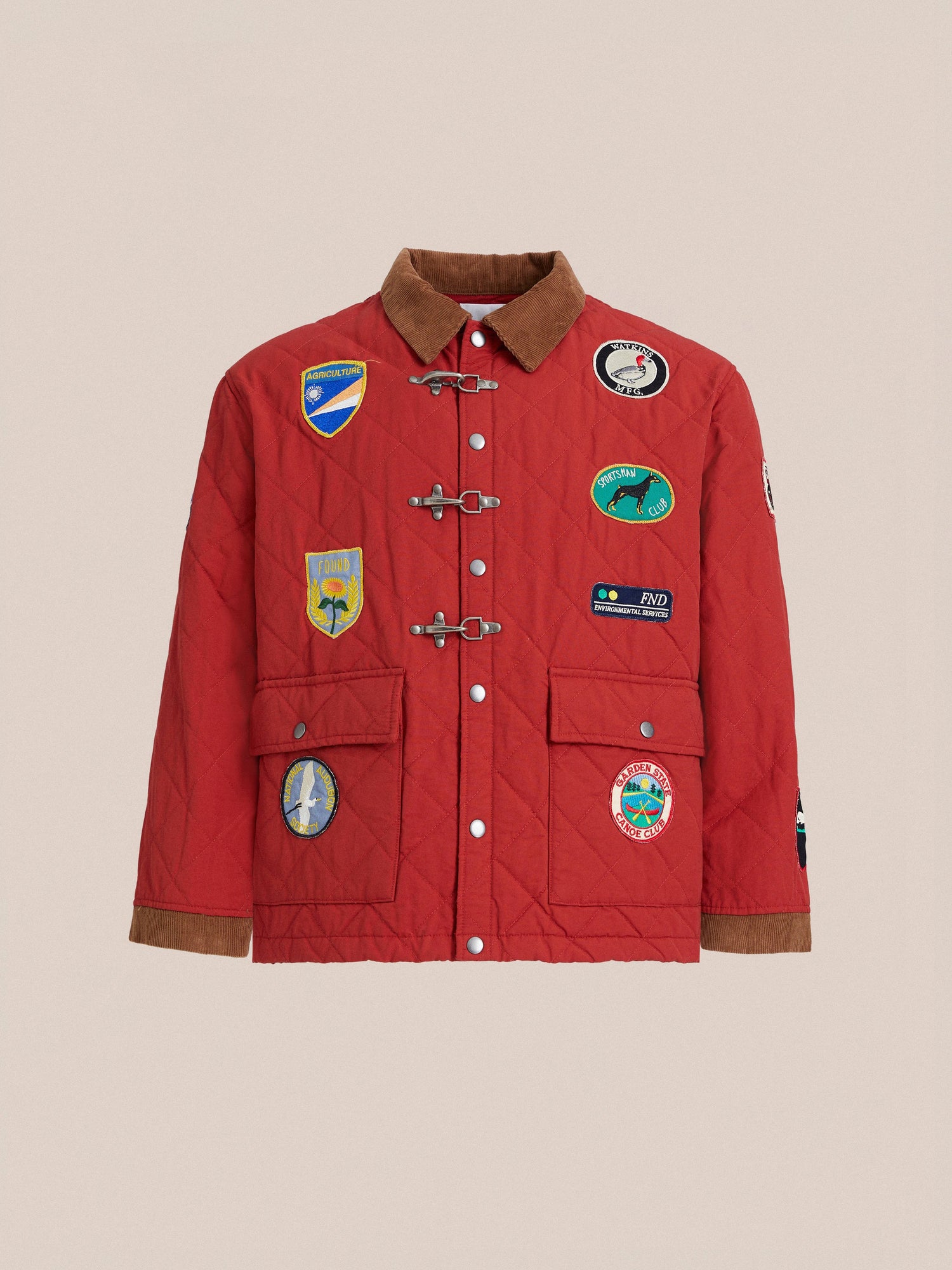 Found's Farmstead Quilt Patch Jacket features a red quilted design with a brown collar and antique silver fireman clasps. Adorned with various embroidered patches on the front, it also has two large front pockets for convenience.