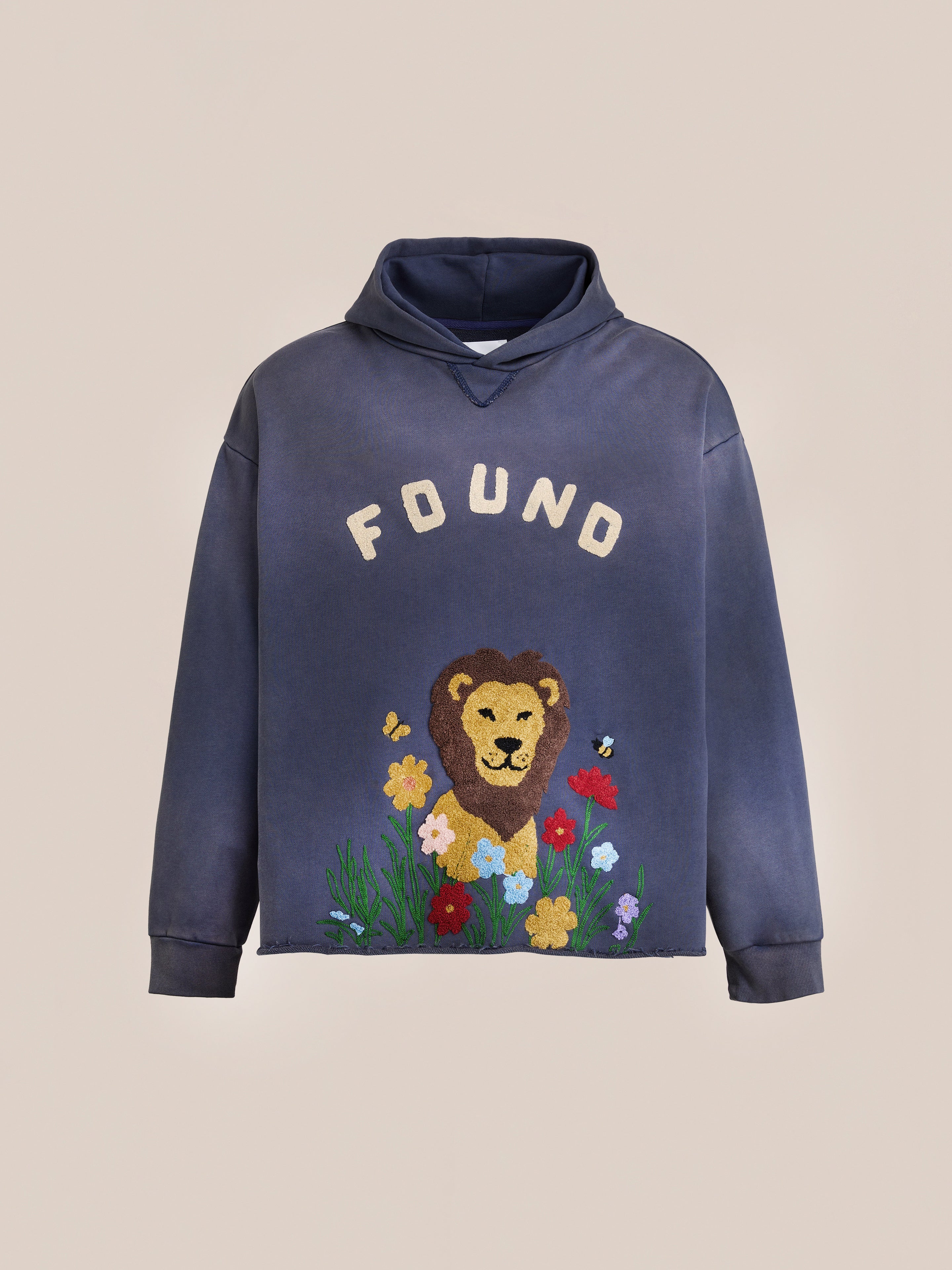 The FOUND Embroidered Wildlife Hoodie in navy features "FOUND" text, a lion face, colorful flowers, and bees embroidered on the front. The hoodie is shown on a plain background.