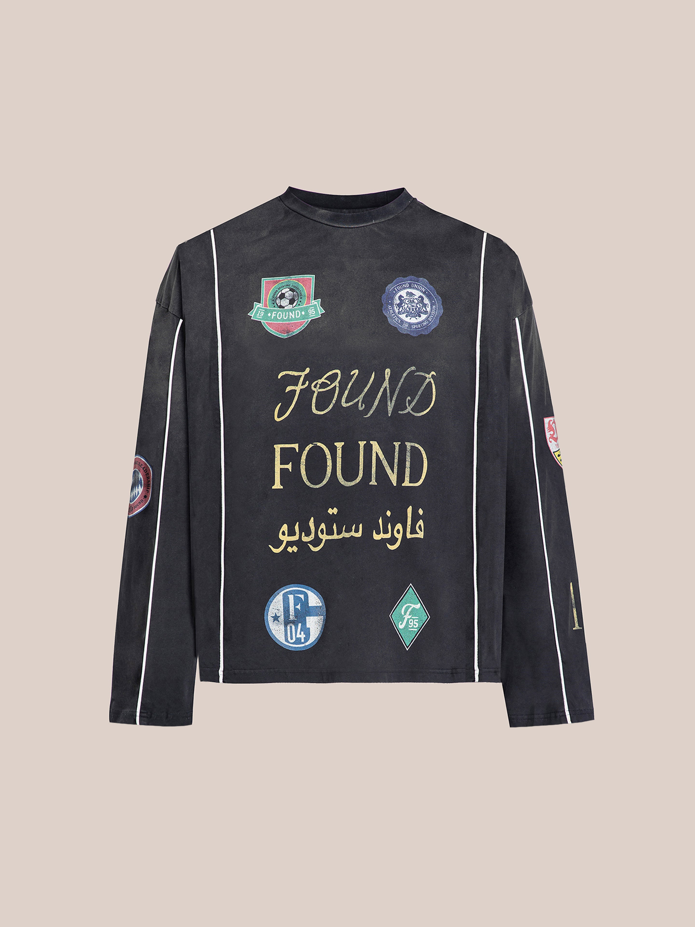 The Multi Language LS Jersey by FOUND is a black long-sleeve jersey adorned with patches and gold "Found" with Arabic text on the front, reflecting a retro football kit style.