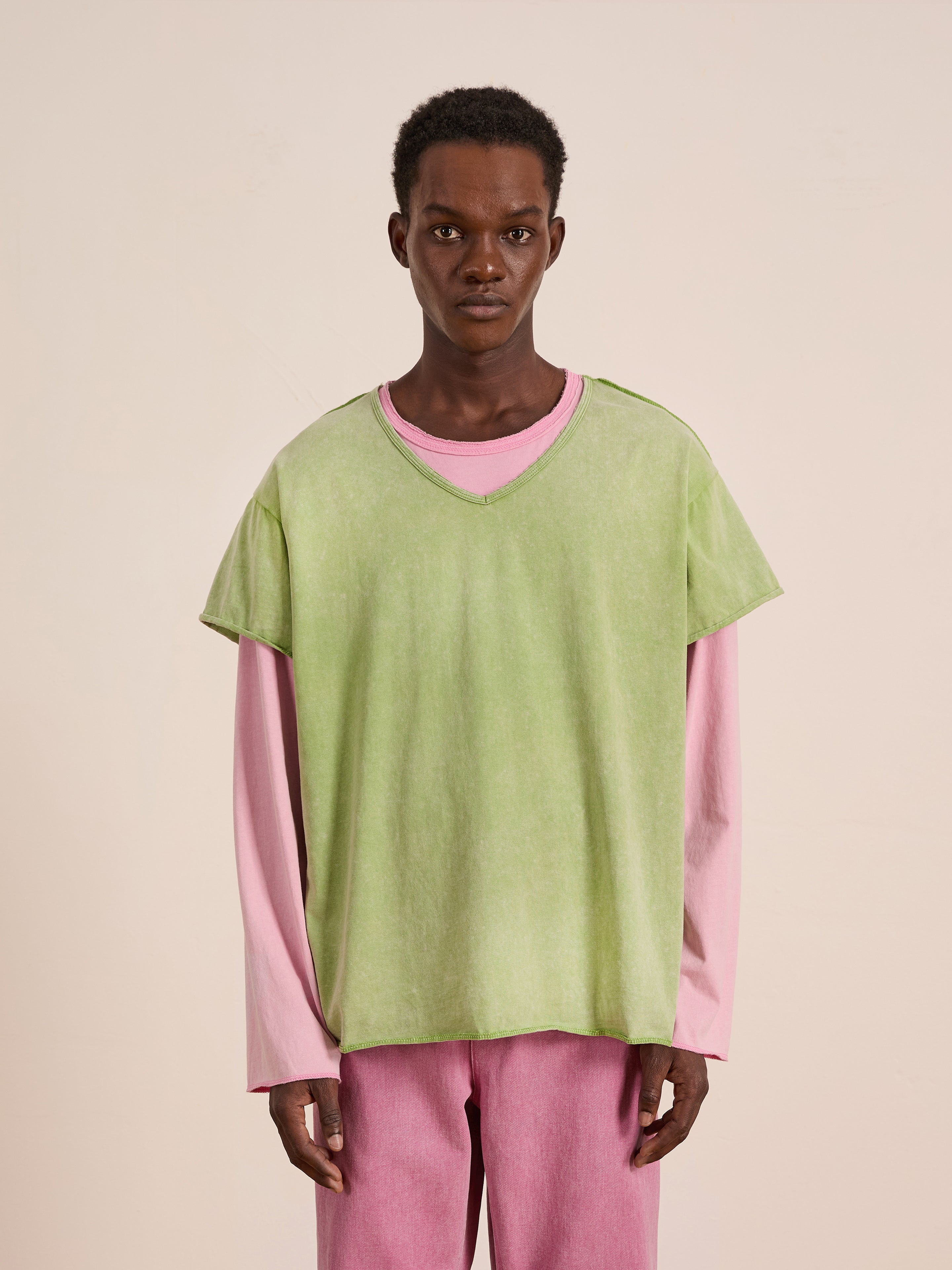 A person wears the FOUND Double Layer LS Tee, featuring a light green t-shirt layered over a pink unisex long sleeve shirt, paired with matching pink pants, against a plain background.