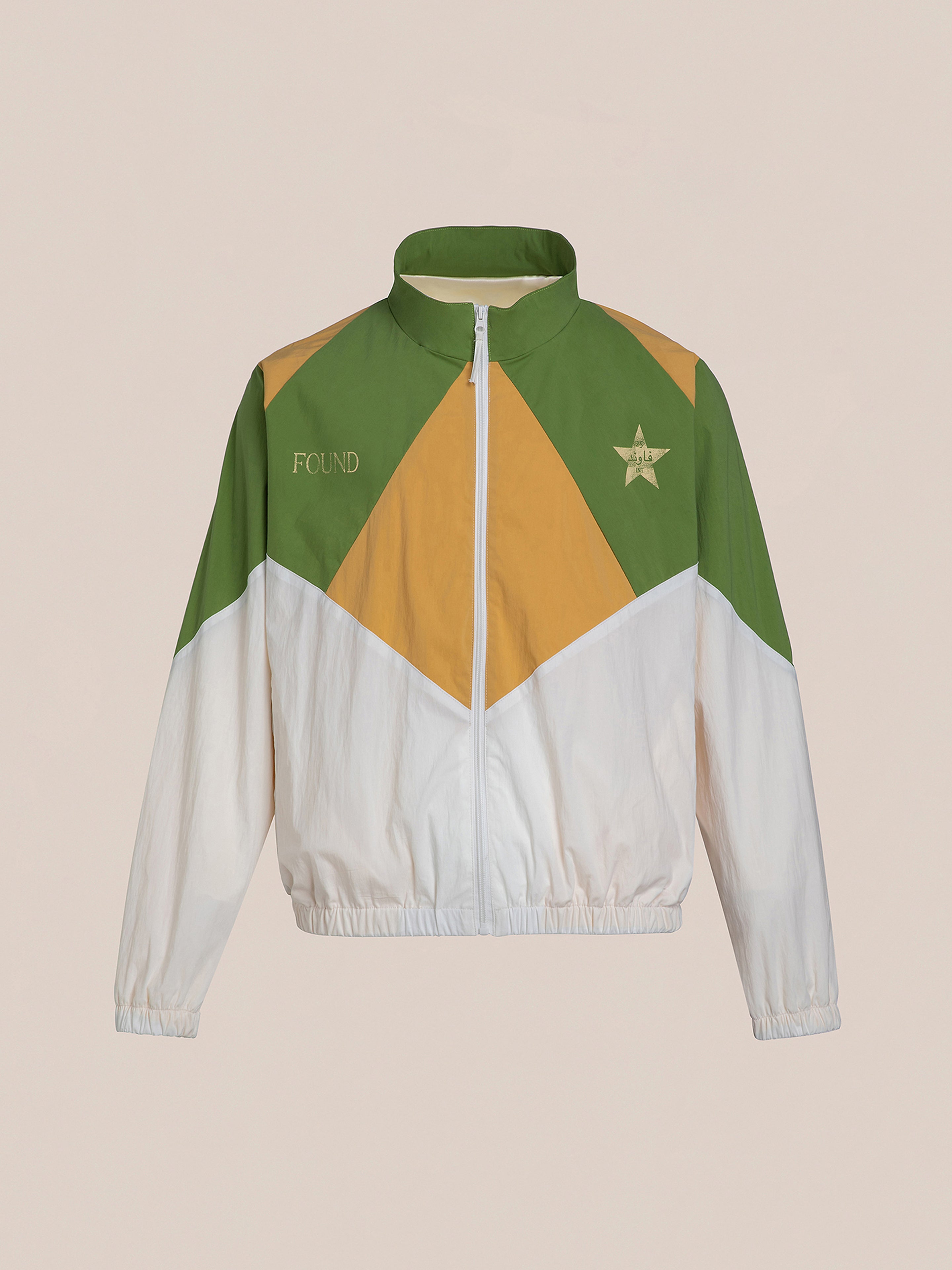 The Legacy Cricket Track Jacket by FOUND is a multicolored windbreaker with white, green, and mustard segments, evoking vintage athletic gear. It includes a zipper, high collar, "FOUND" embroidered on the left, and a star emblem on the right.