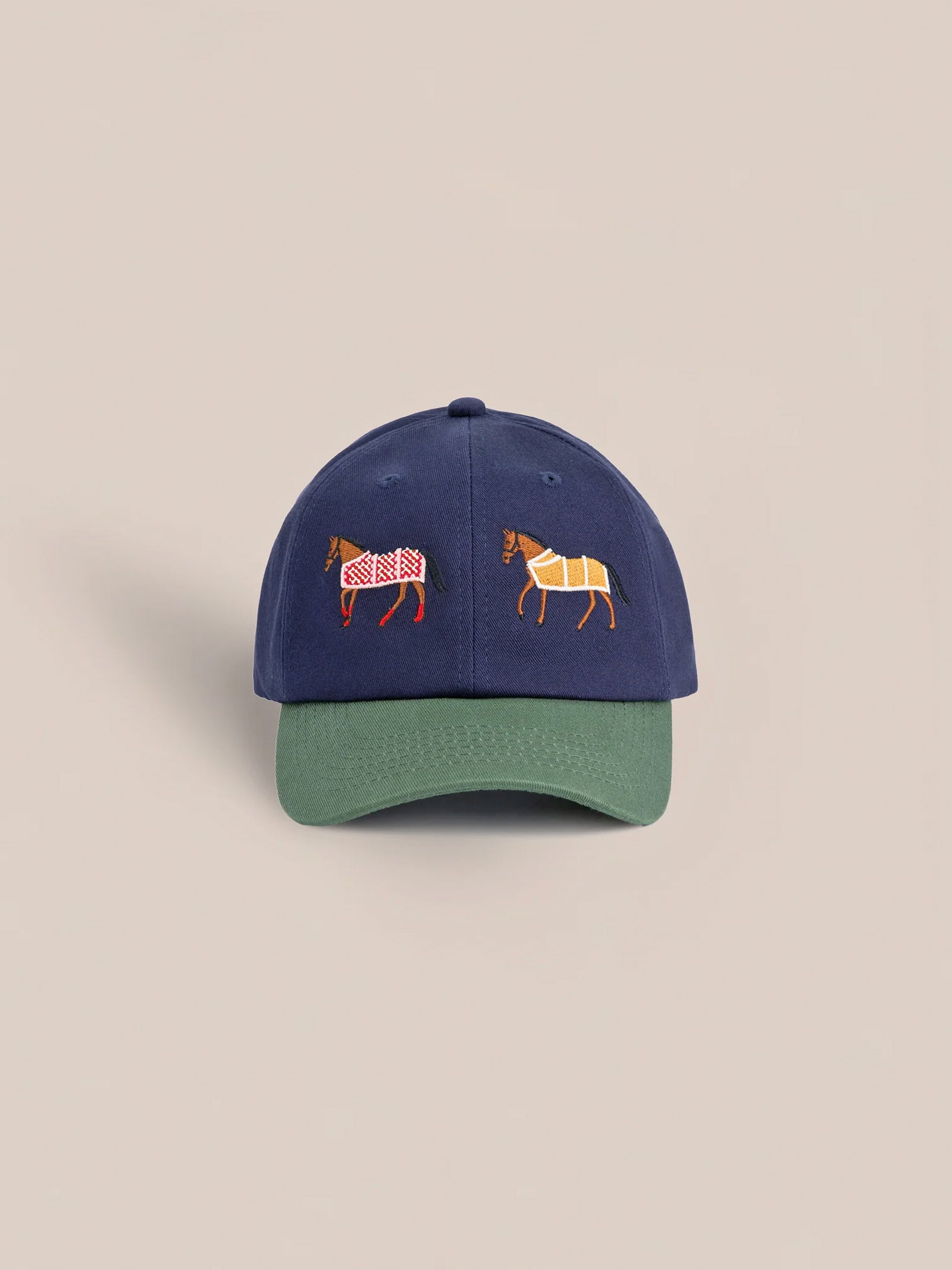The Found Horse Equine Cap embodies 70's color-blocking with a navy blue crown and green brim, adorned with embroidered images of two horses in checked racing blankets.