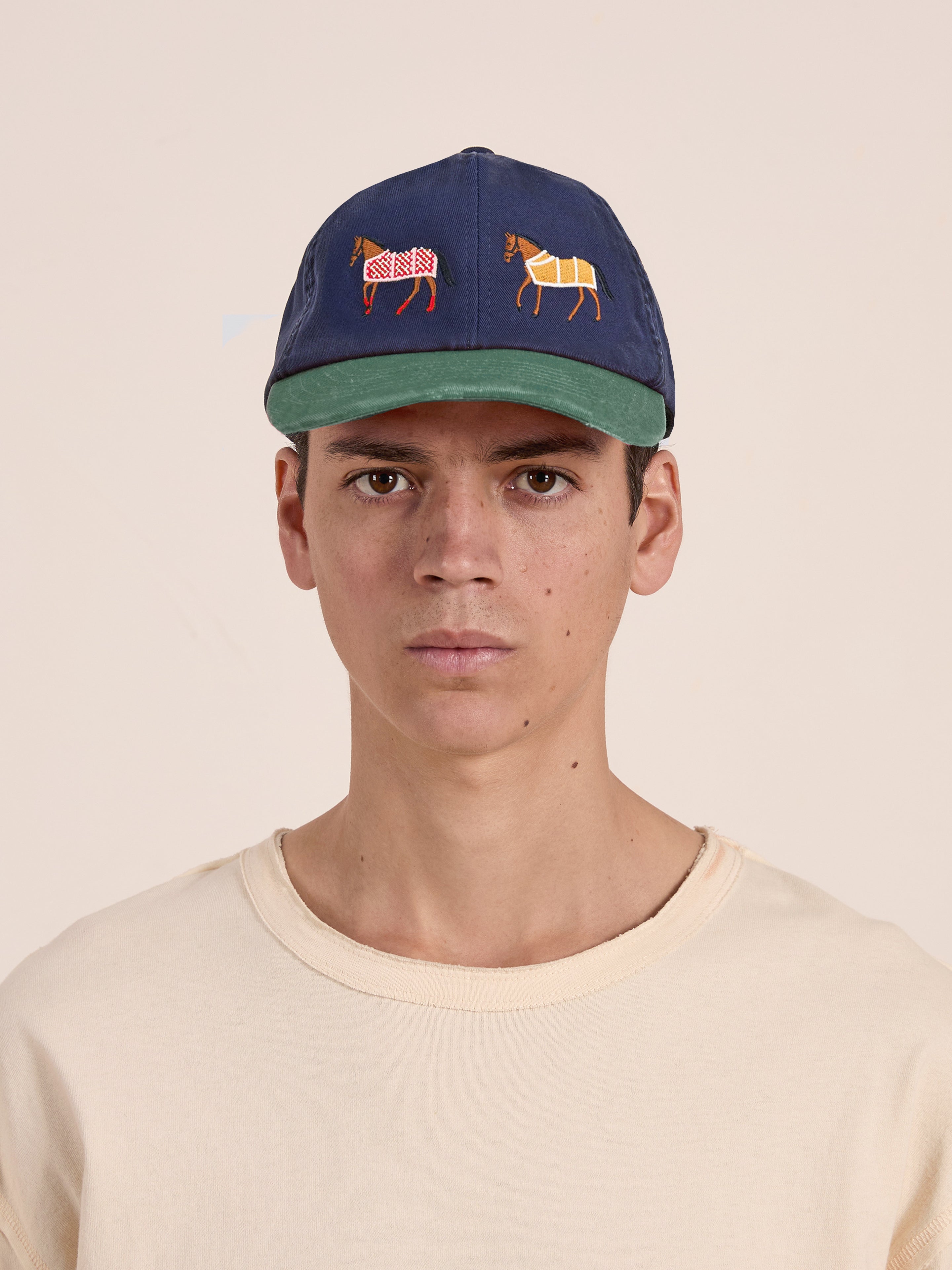 A person wearing a beige shirt and a stylish Found Horse Equine Cap, featuring embroidered animal designs on the front.