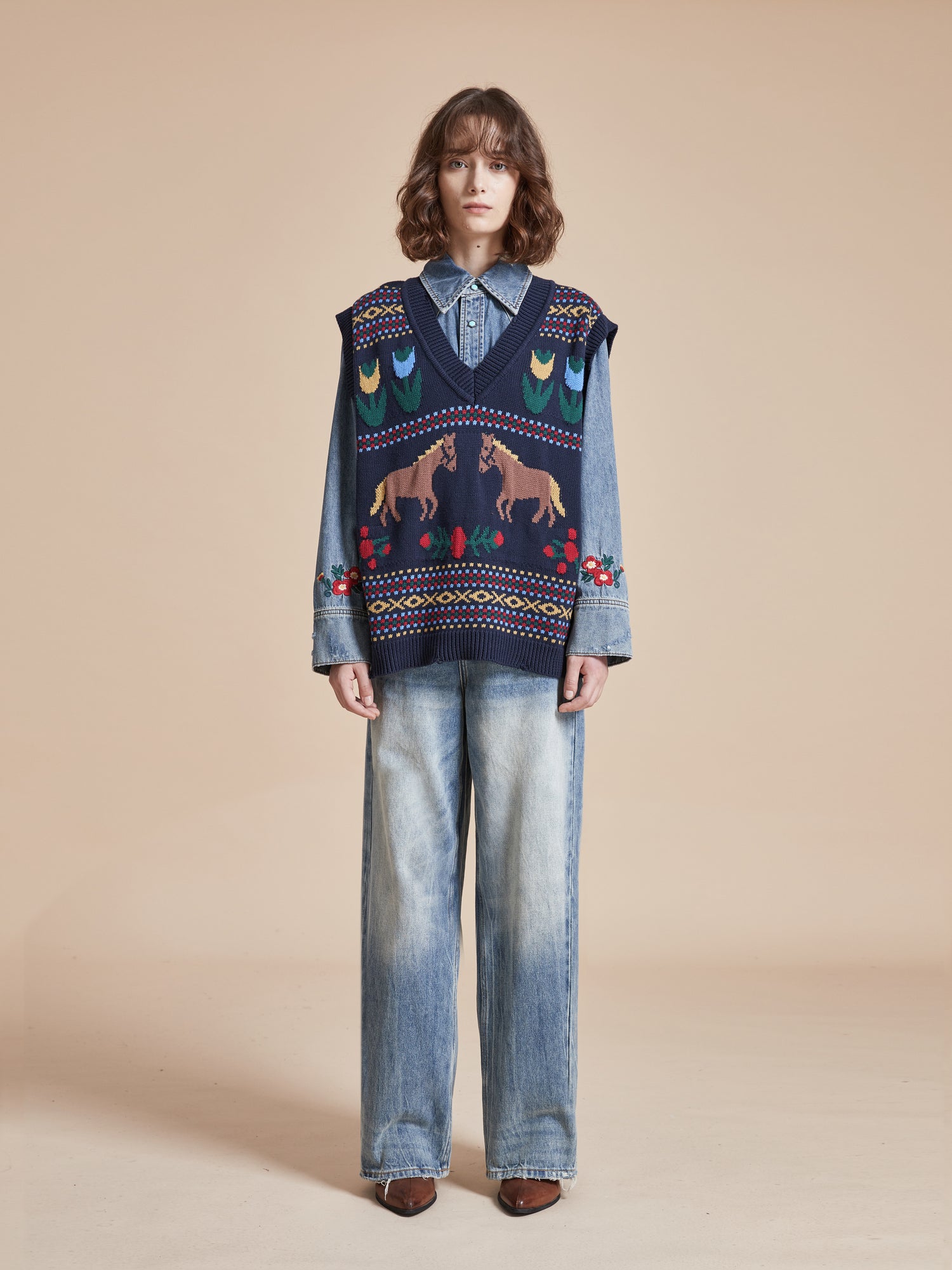 The model is wearing a Found Isle Horse Reverie Sweater Knit Vest and jeans.