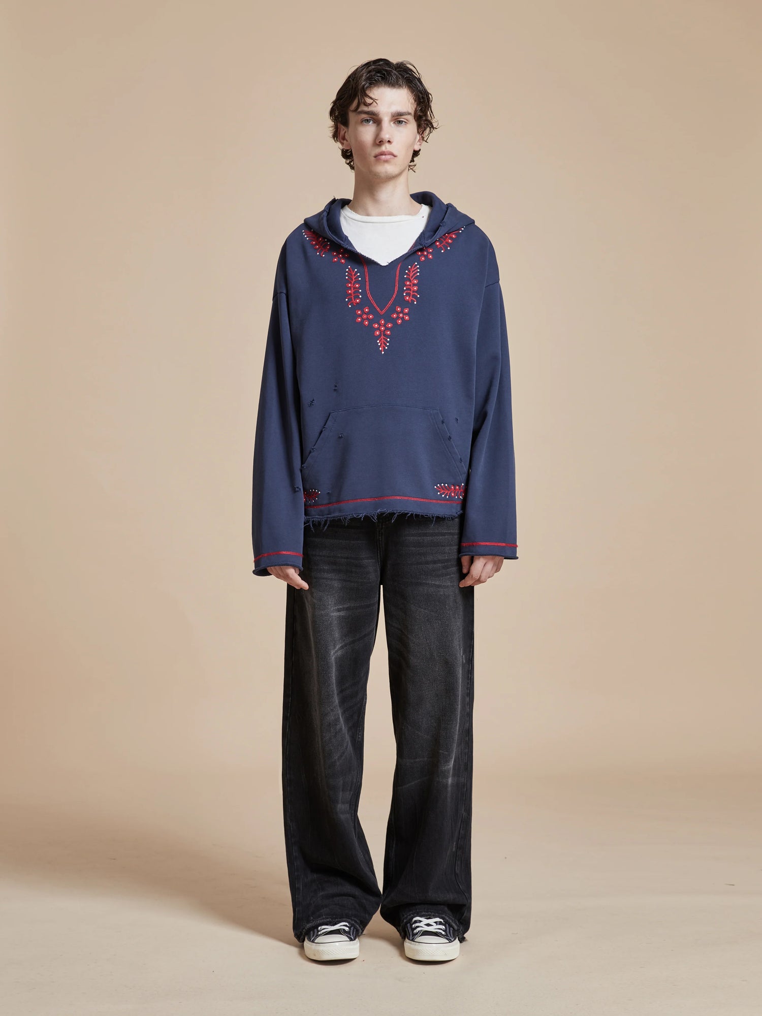 A man wearing a Found Indus Embroidered Hoodie with motifs and Phulkari embroidery, paired with black pants.