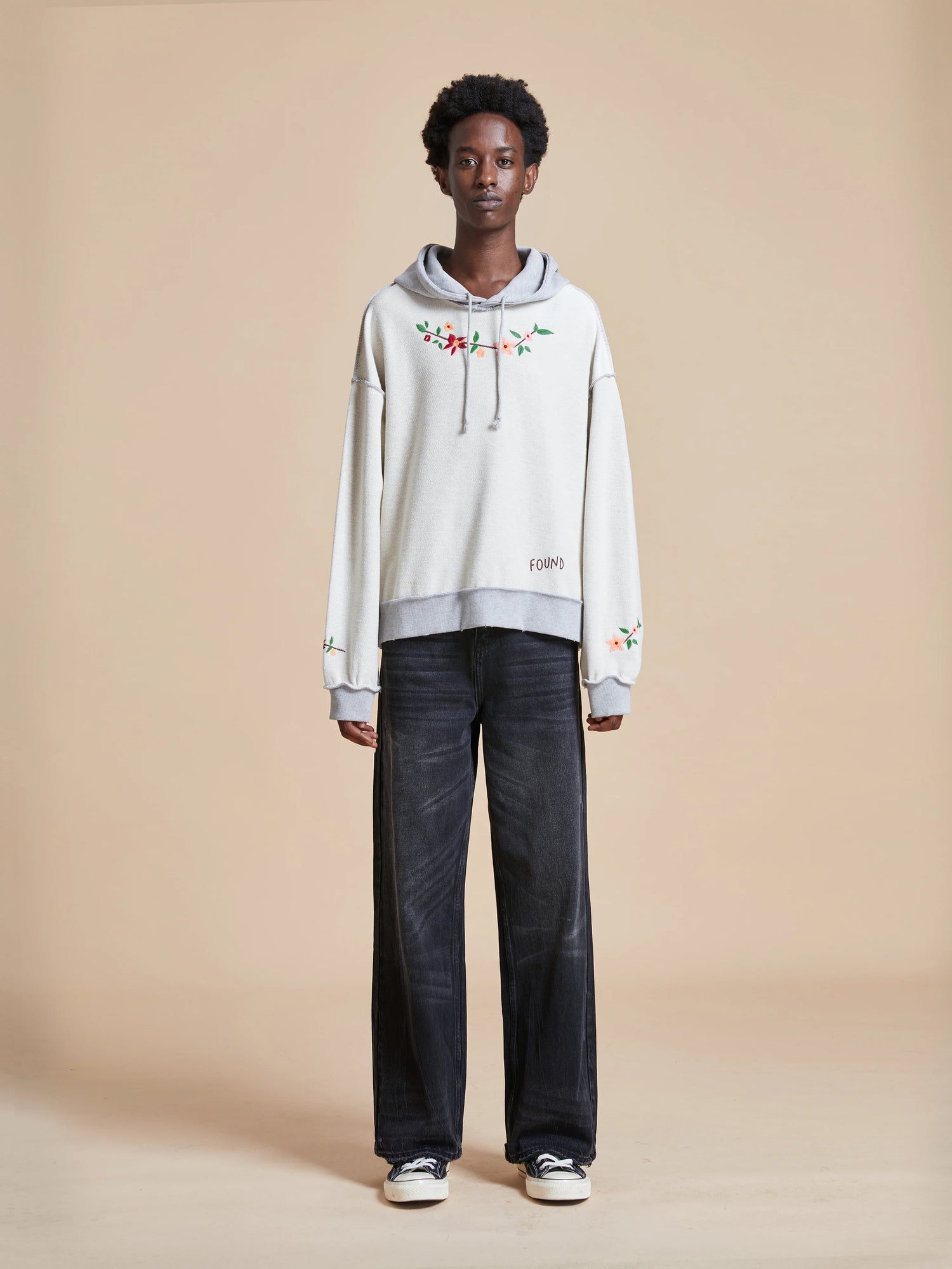 A man wearing a Found Inverse Flower Petal Hoodie made of french terry fabric and black pants.