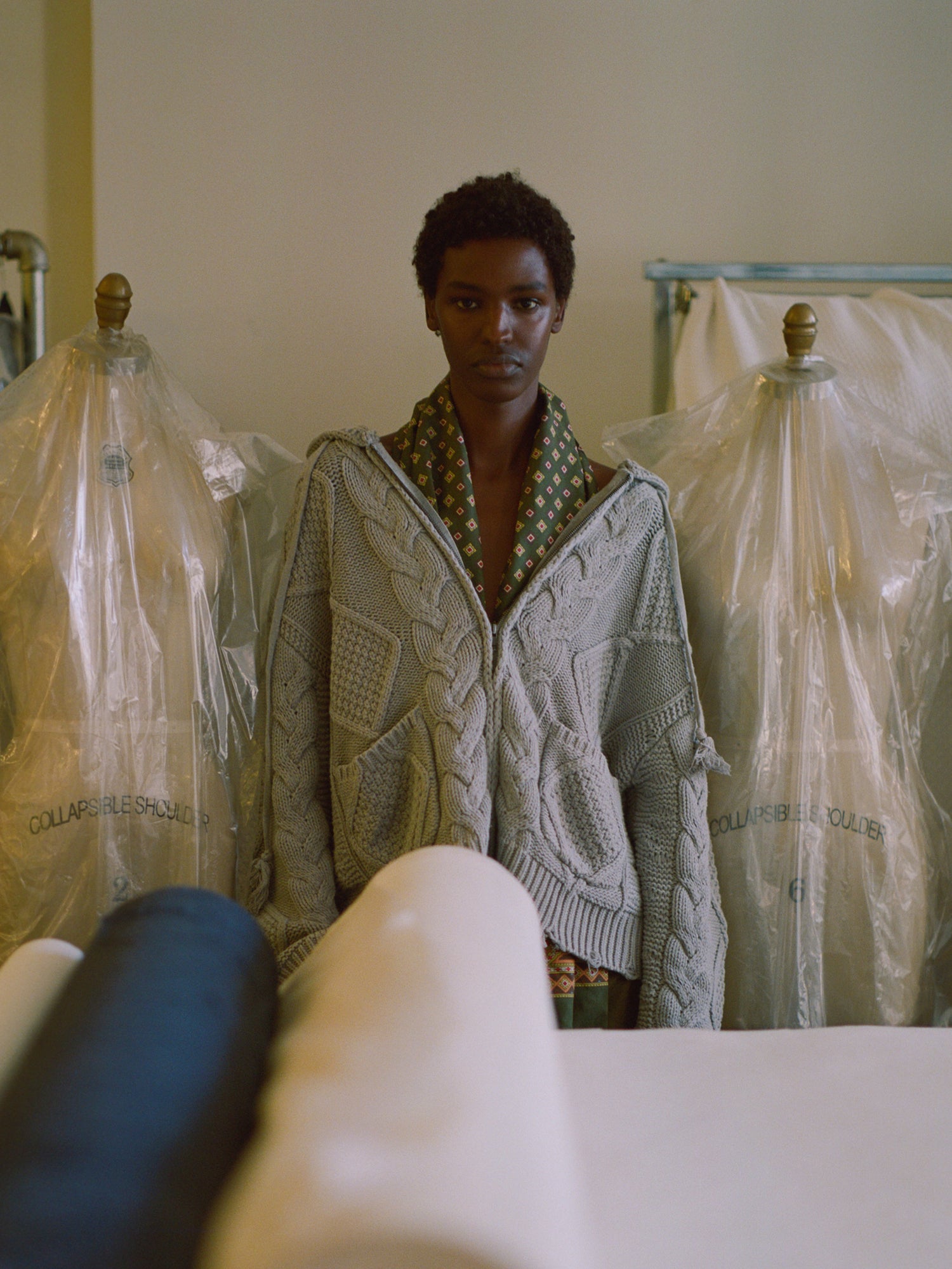 A man wearing a Zip Up Distressed Cable Knit Hoodie by Found standing in front of mannequins.