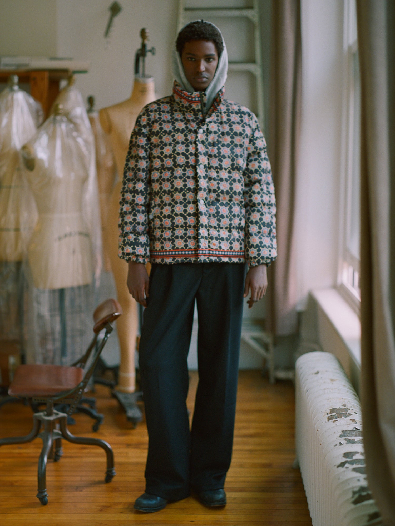 A man in a hooded Found Ajrak Block Puffer Jacket standing in a room.