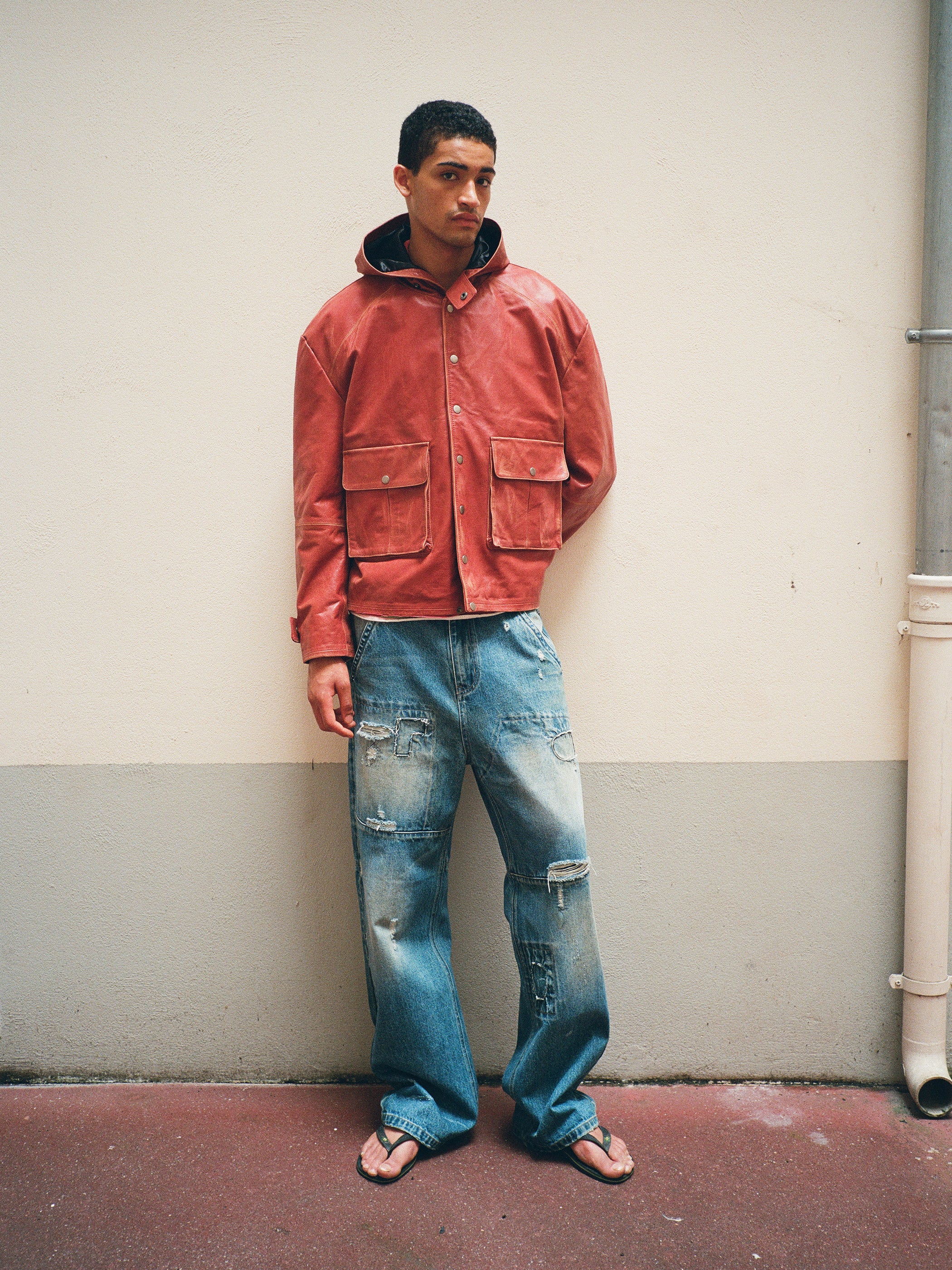 A person stands against a wall, wearing the FOUND Distressed Leather Pocket Hoodie.