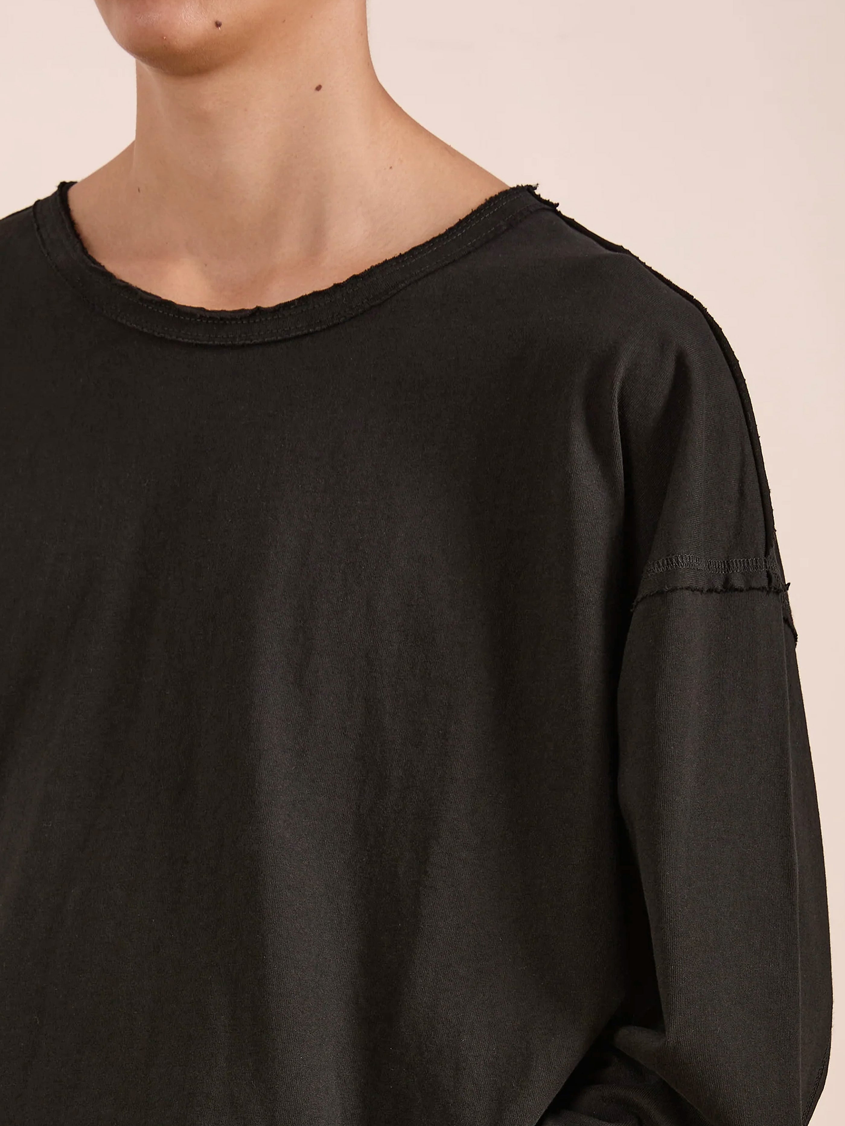 Model wearing the FOUND Reversed LS Tee, a black long sleeve with relaxed fit, raw deconstructed neckline, and visible shoulder seam. Shown from shoulders up.