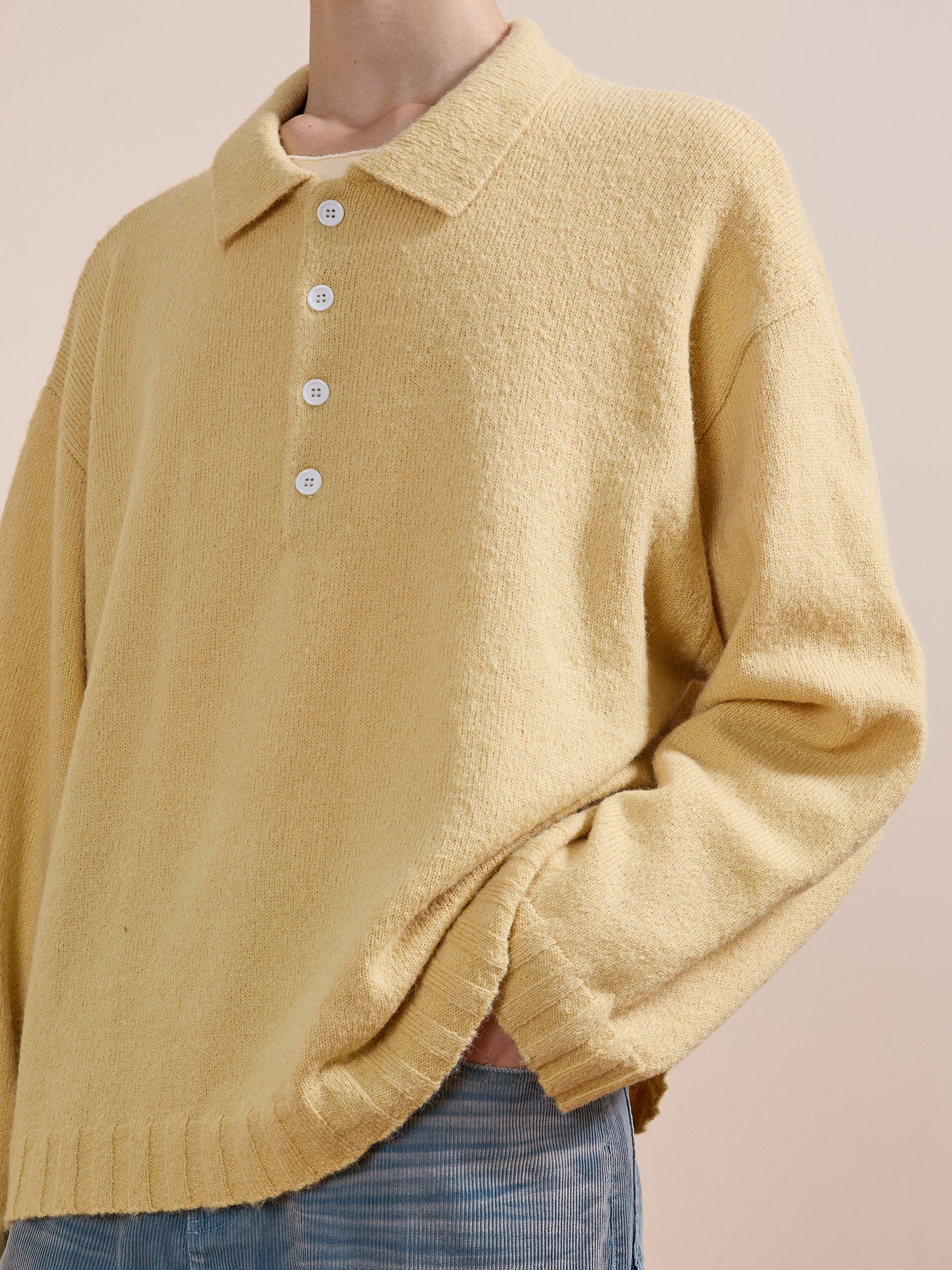 Model wears the FOUND Knit LS Polo Sweater in yellow, made from soft brushed knit with white buttons, styled with light blue pants against a plain background.