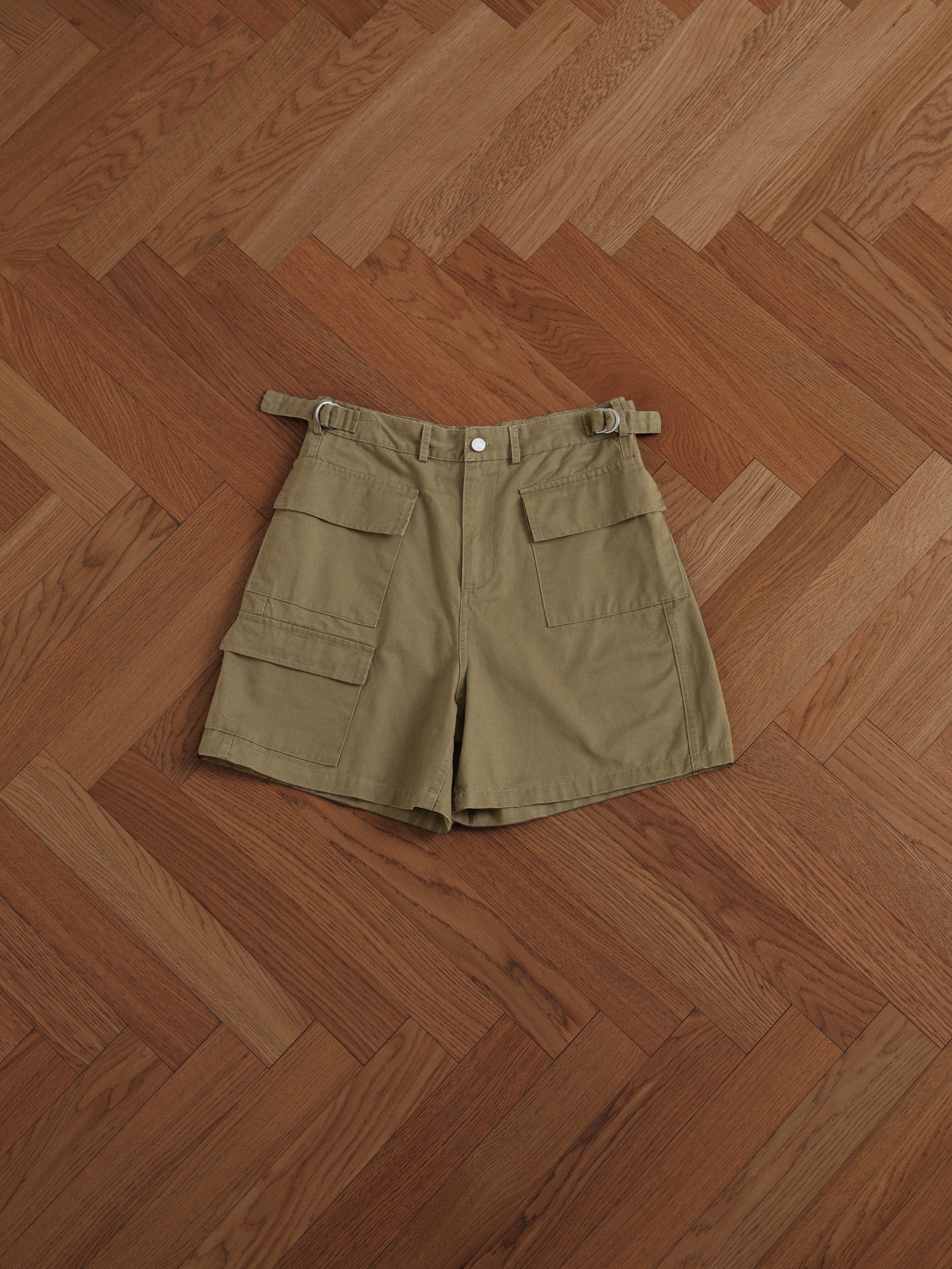 A pair of Found Twill Cargo Shorts with cargo pockets on a wooden floor.