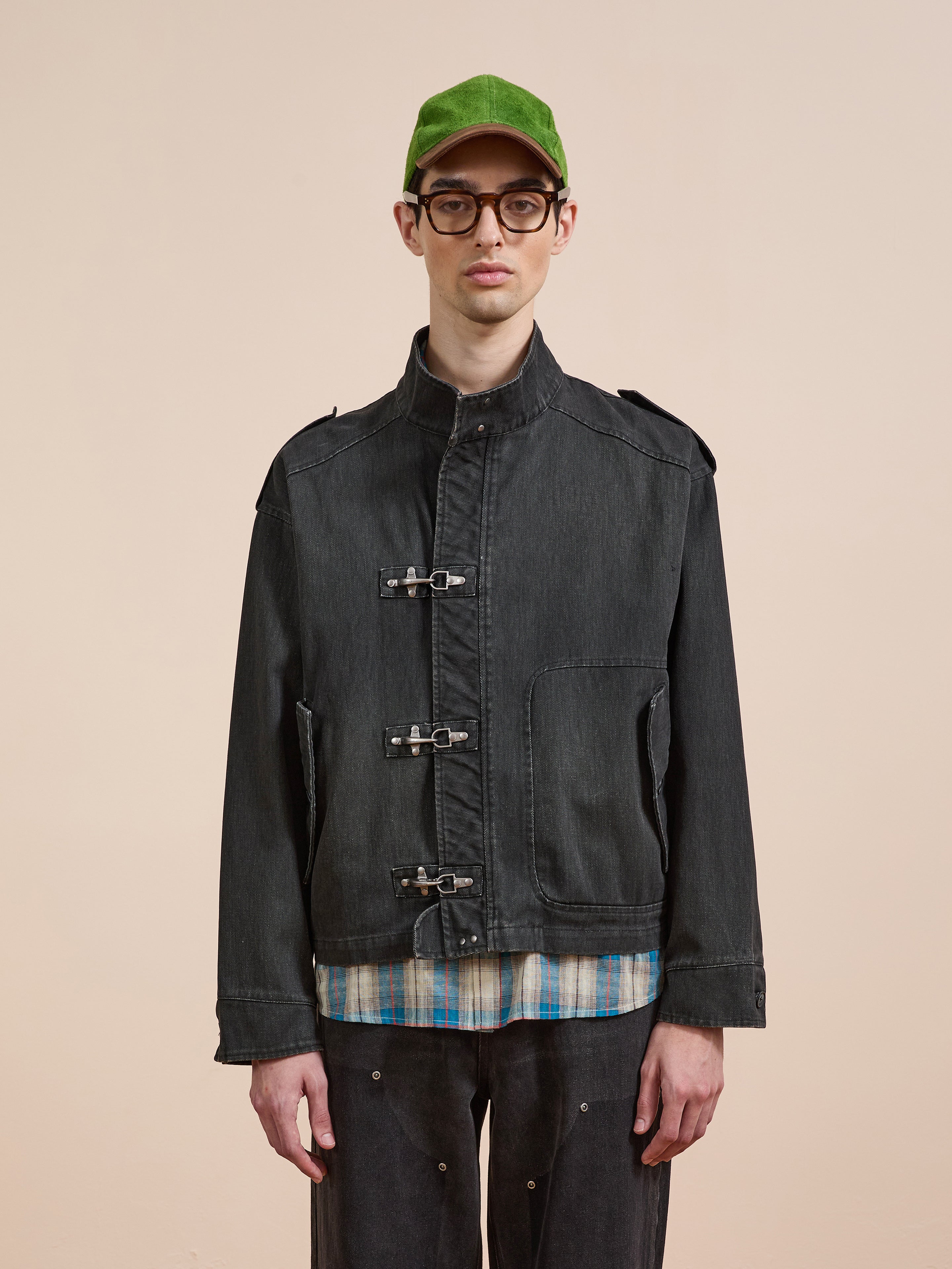 A person wearing a green cap, glasses, and the Found Utility Clasp Work Jacket over a plaid shirt stands against a plain beige background.