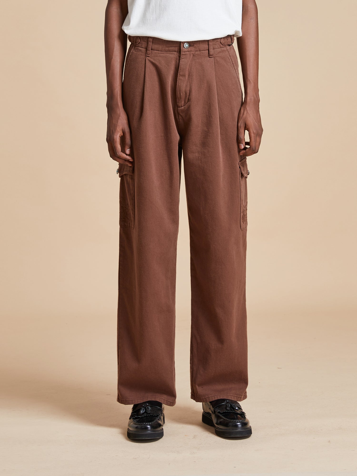 A man wearing Found Dusky Western Cargo Jeans, a classic silhouette with brown pants and a white t-shirt.
