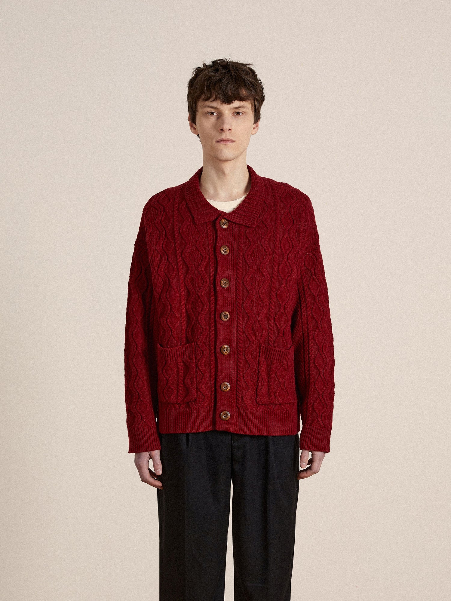 A man wearing a red Parsidan Cable Knit Cardigan and black pants by Found.