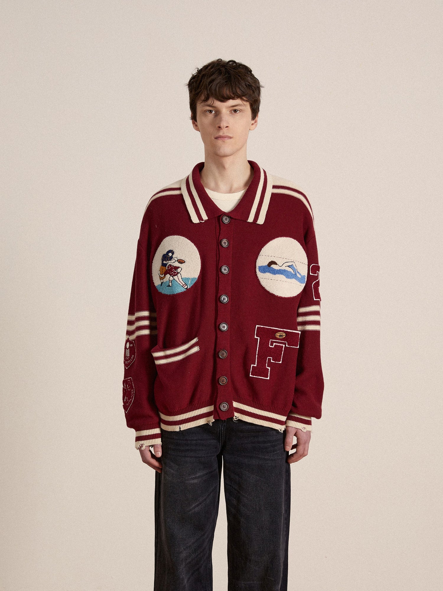 A man wearing a burgundy Found Varsity Patch Collared Cardigan and jeans, emblematic of vintage Ivy League fashion.