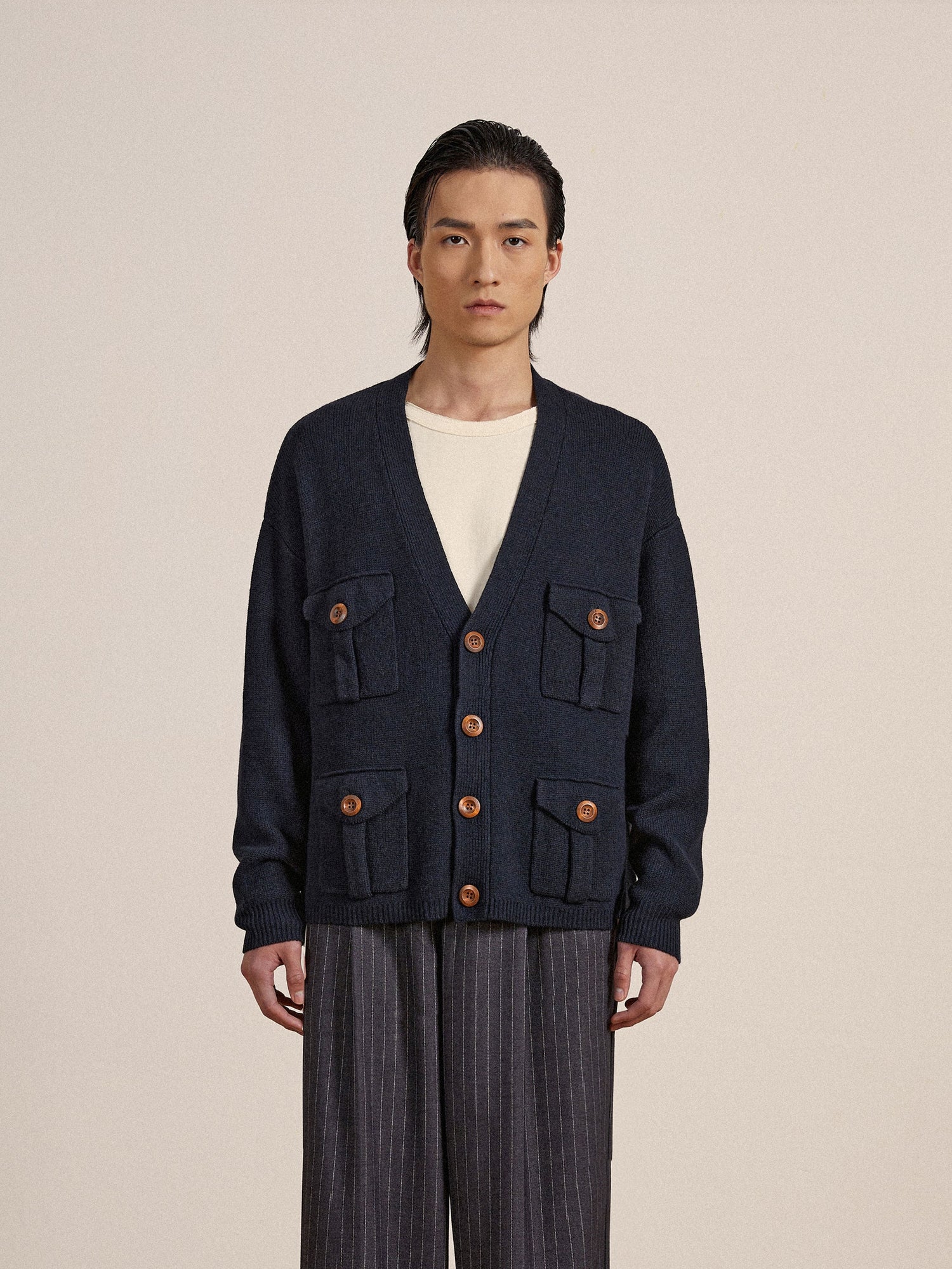 A man wearing a navy knit fabric Found Multi Pocket Cardigan with wooden buttons and pants.