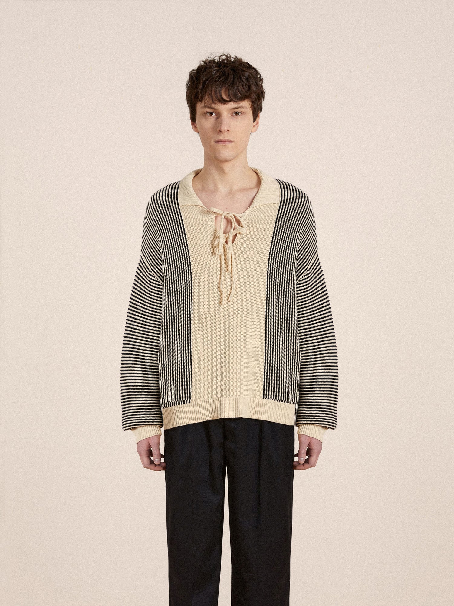 The model is wearing an intricate knit patterns Found Tabas Tie Knit Collared Sweater and black pants.